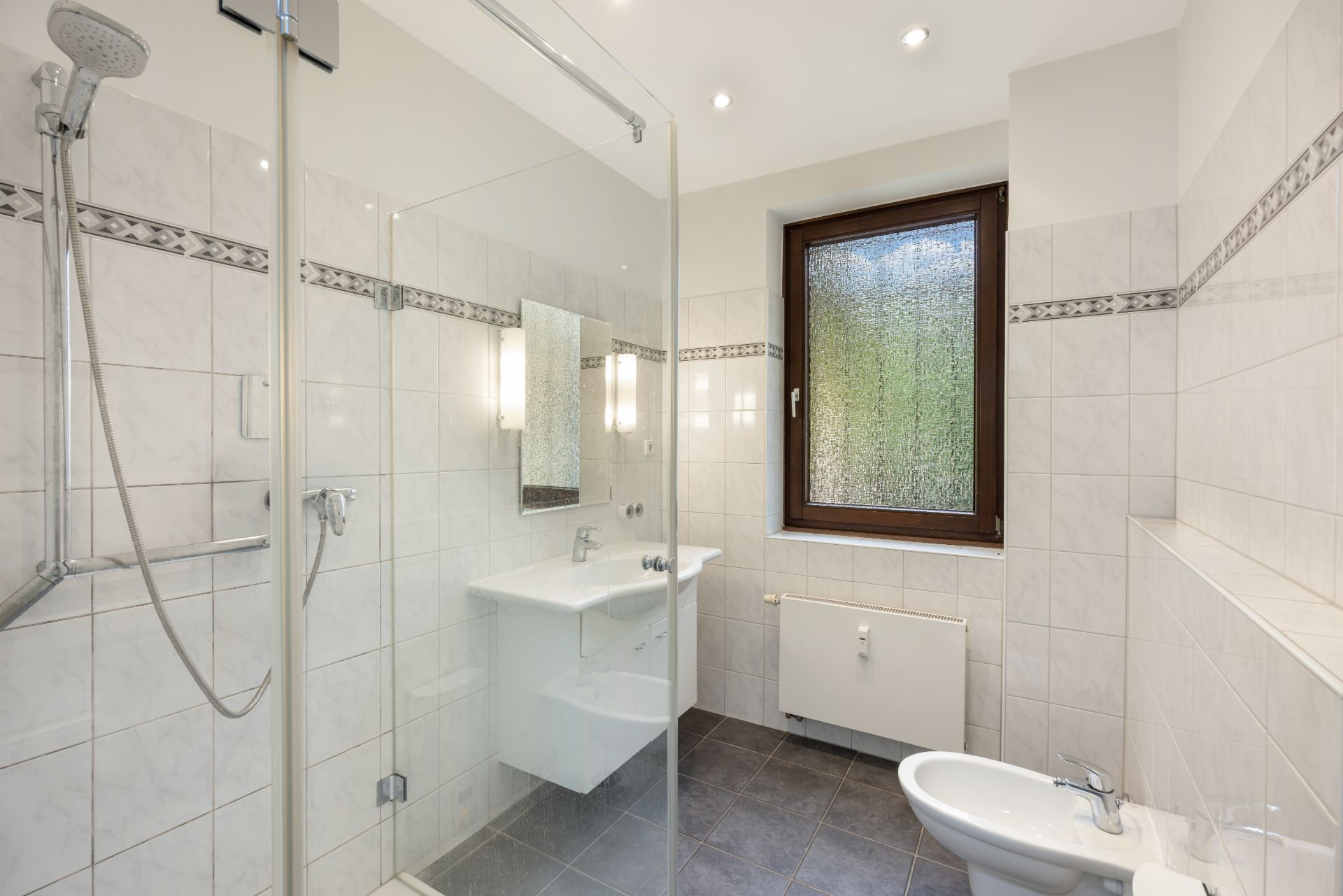 Modernes Badezimmer mit Dusche, Waschbecken, Fenster und Bidet.