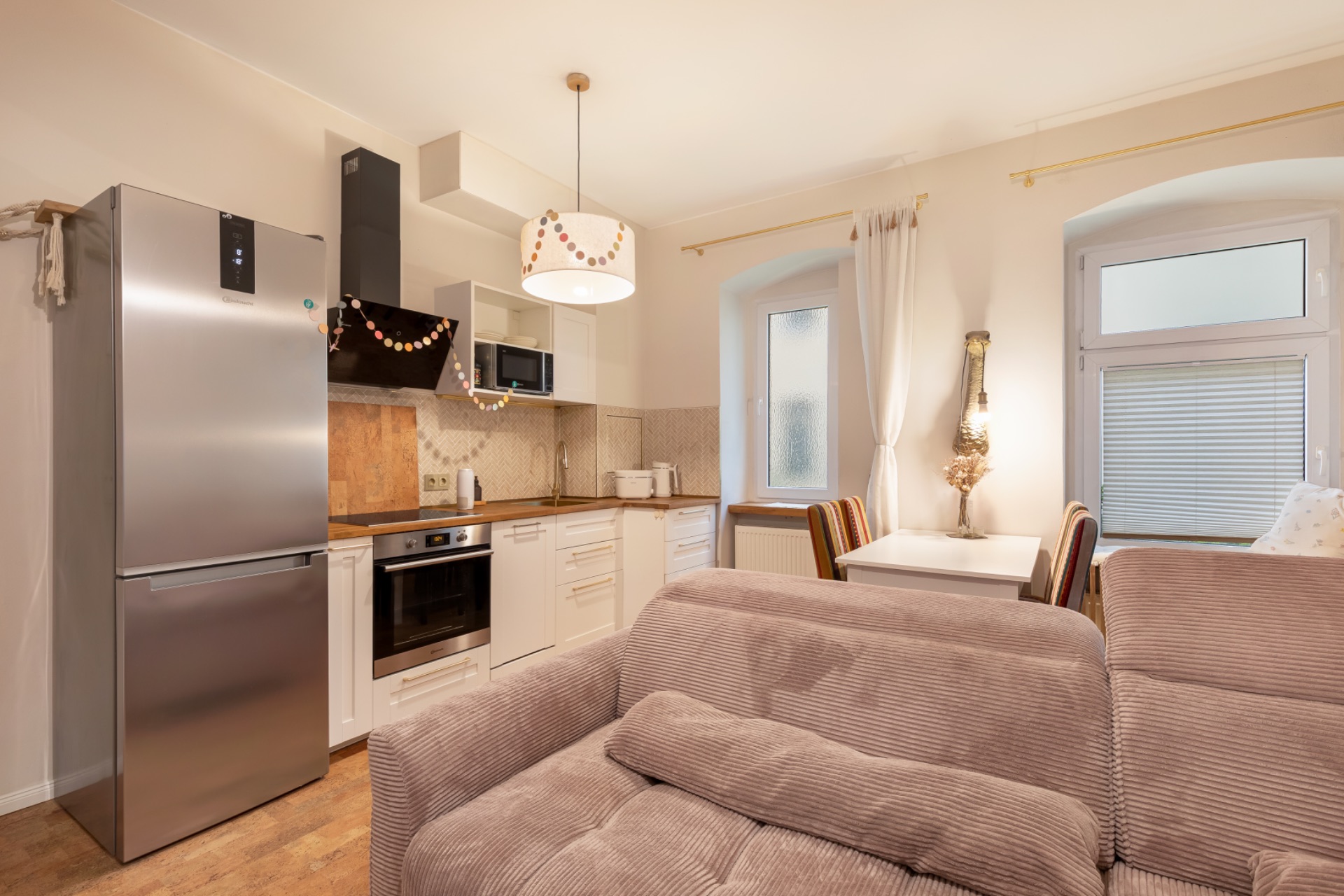 Helle Wohnküche mit Sofa, Esstisch, Einbauküche und großem silbernen Kühlschrank.