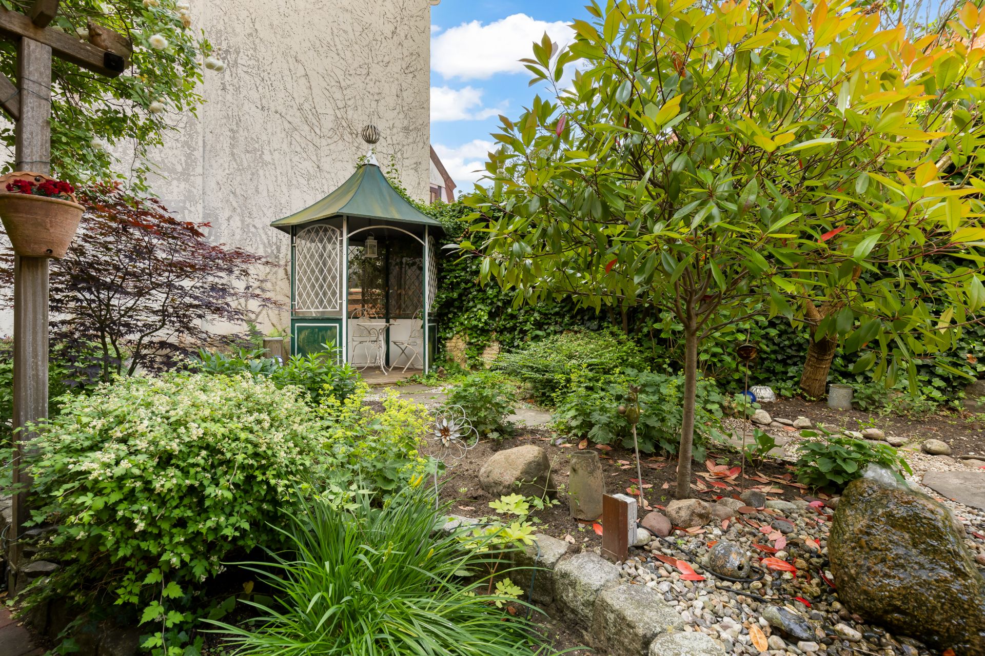 Grüner Garten mit Pavillon, Sträuchern, Bäumen und Steinen.
