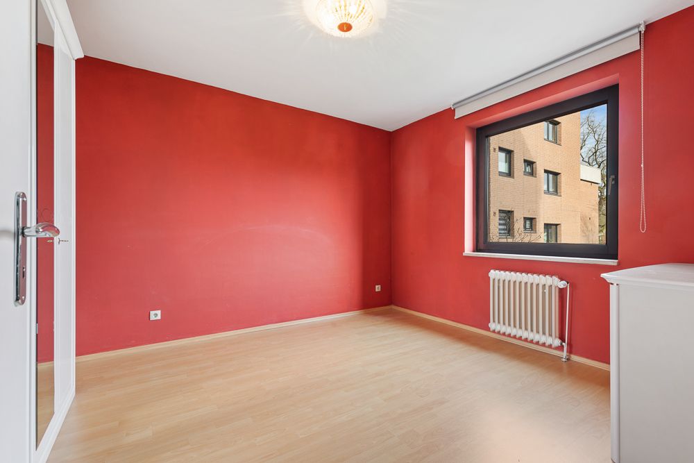 Leerer Raum mit roten Wänden, großem Fenster, Heizung und hellem Holzboden.