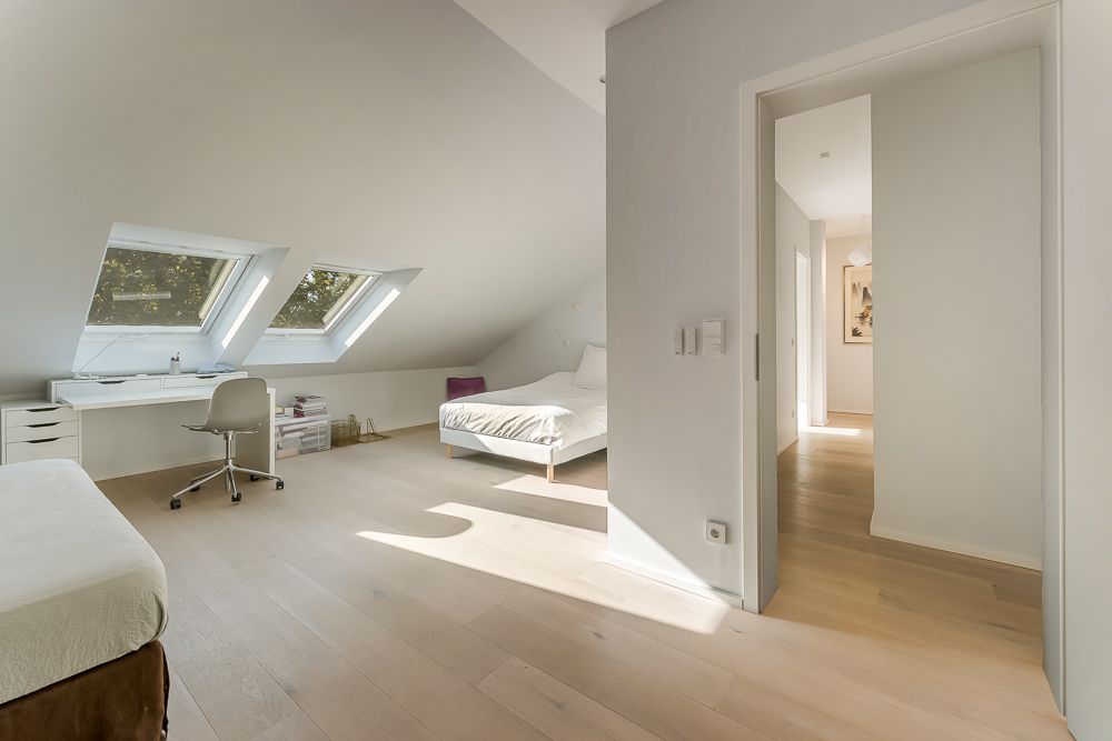 Helles Schlafzimmer mit Schreibtisch, zwei Fenstern im Dach und Holzboden.