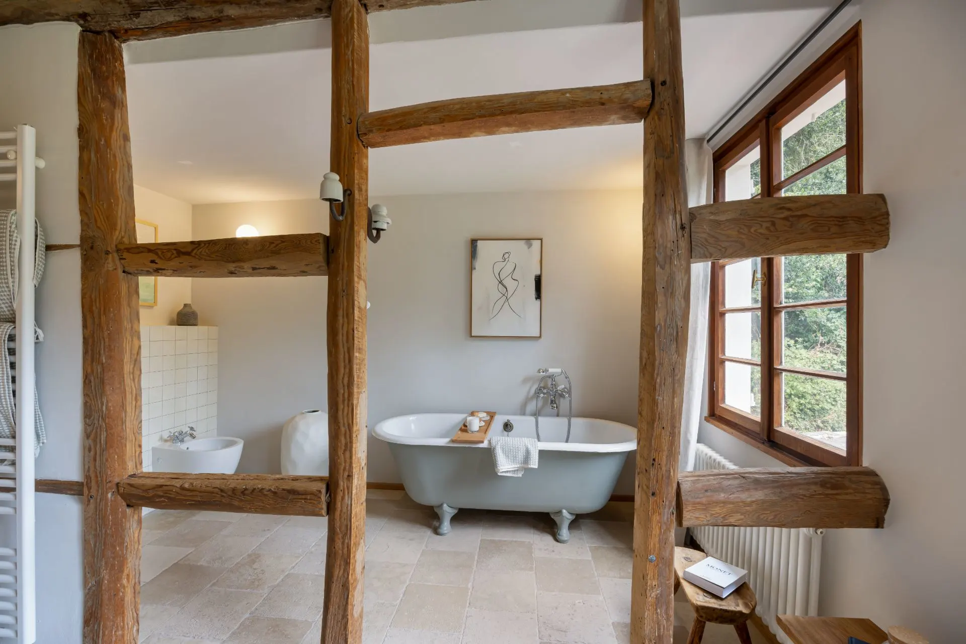 Helles Badezimmer mit freistehender Badewanne, Holzbalken und großem Fenster.