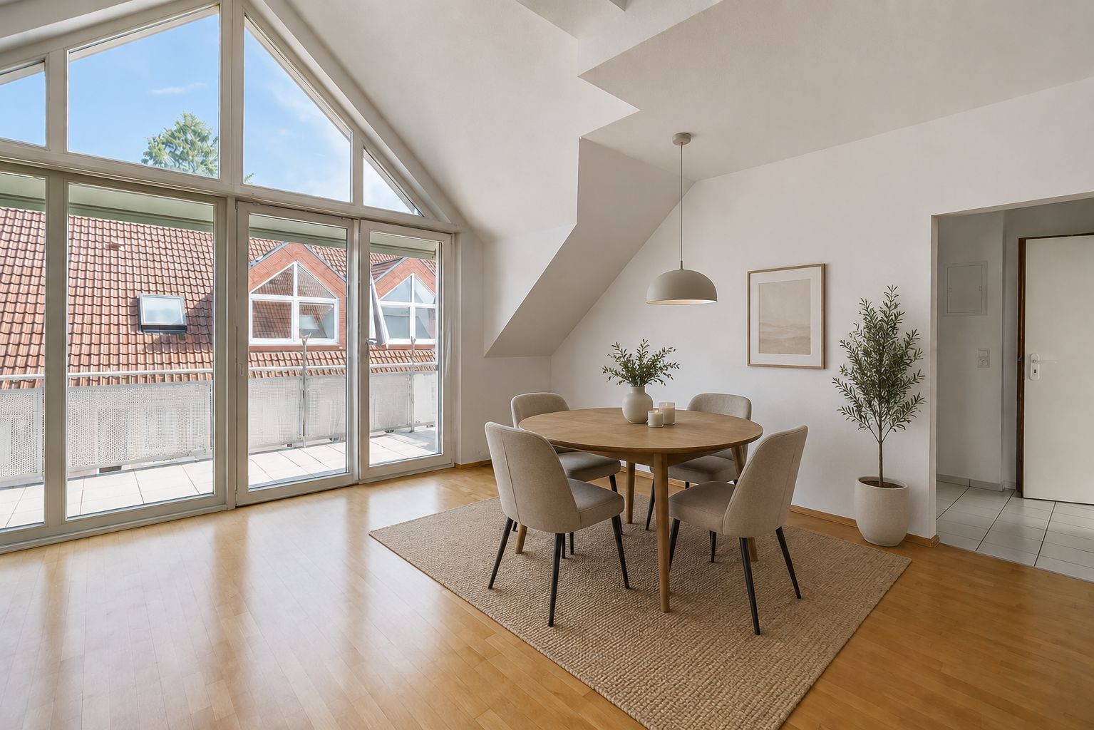 Helles Esszimmer mit rundem Tisch, fünf Stühlen, großen Fenstern und Pflanzen auf Parkettboden.