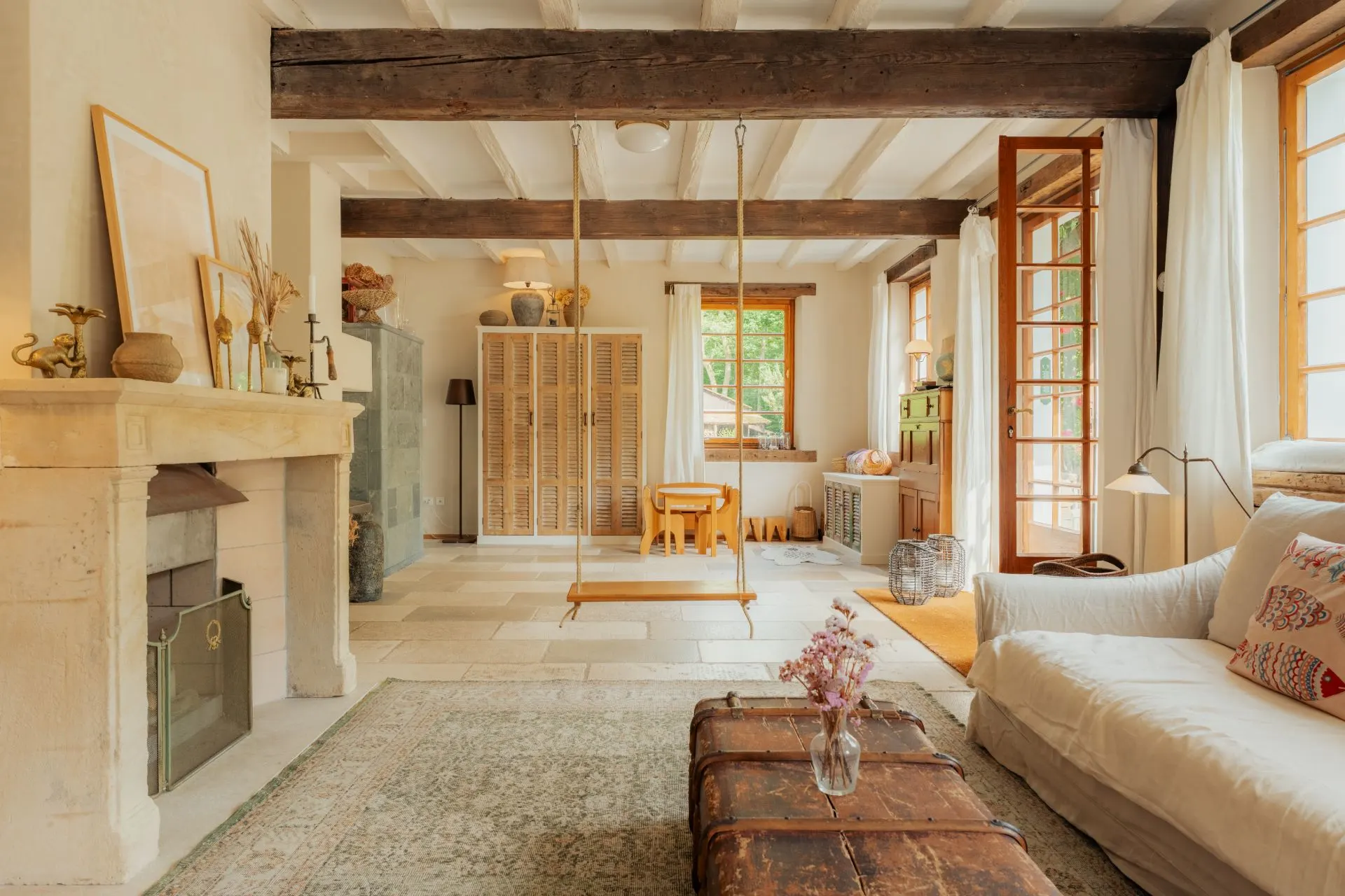 Helles Wohnzimmer mit Kamin, Schaukel, Sofa, Holzbalken und großen Fenstern.