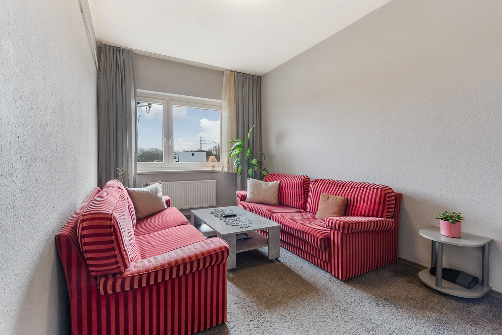 Wohnzimmer mit zwei rot gestreiften Sofas, Couchtisch, Fenster und Zimmerpflanze.