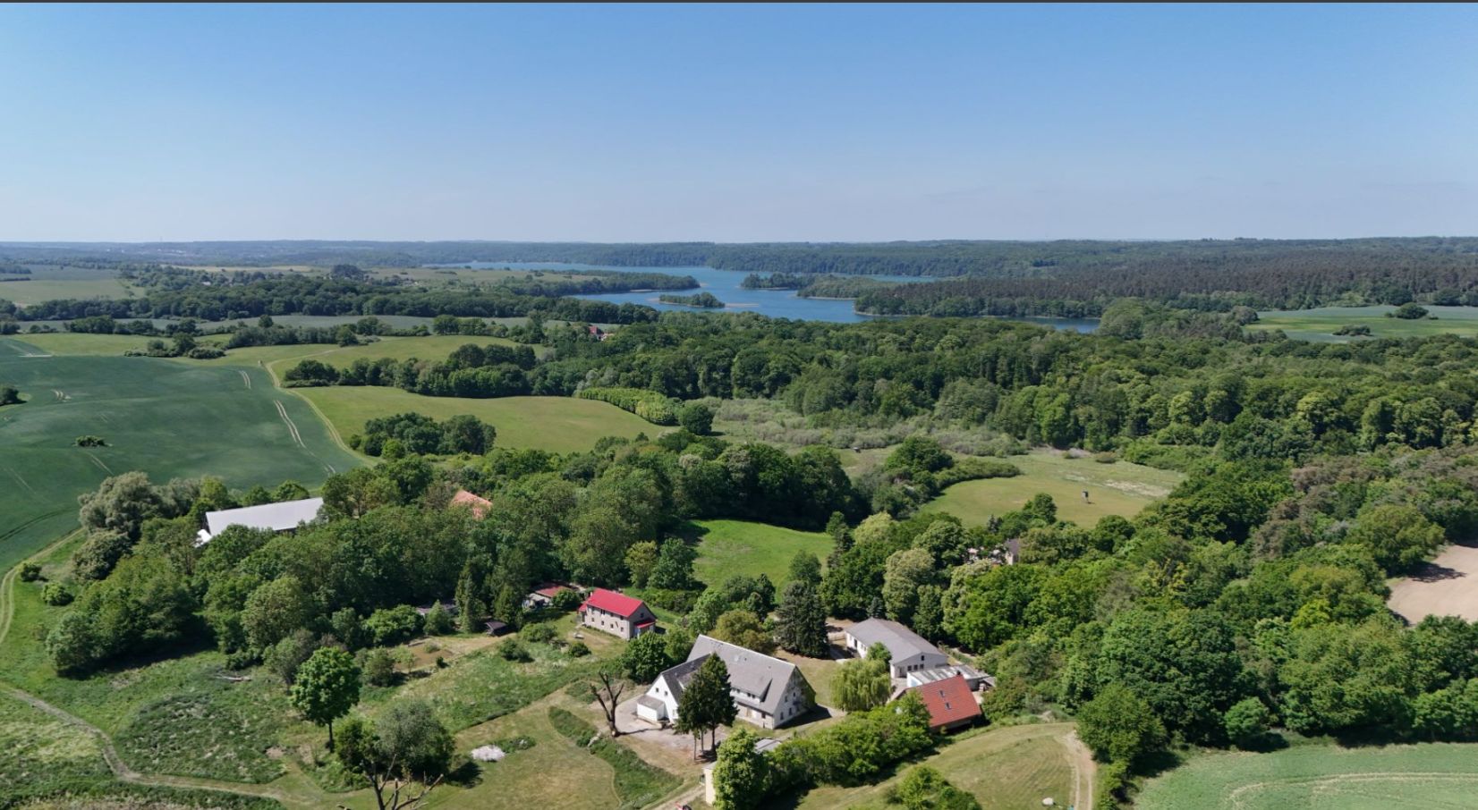 Luftaufnahme von mehreren Wohnhäusern und viel grüner Landschaft mit einem See im Hintergrund.