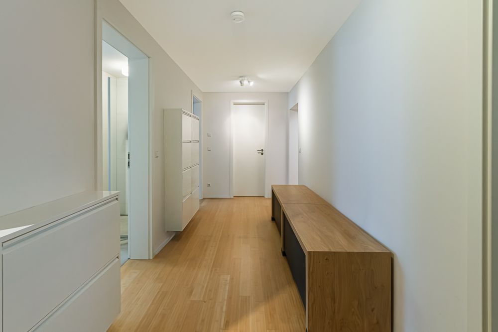 Heller Flur mit Holzboden, weißen Schränken und einer Holzbank an der Wand.