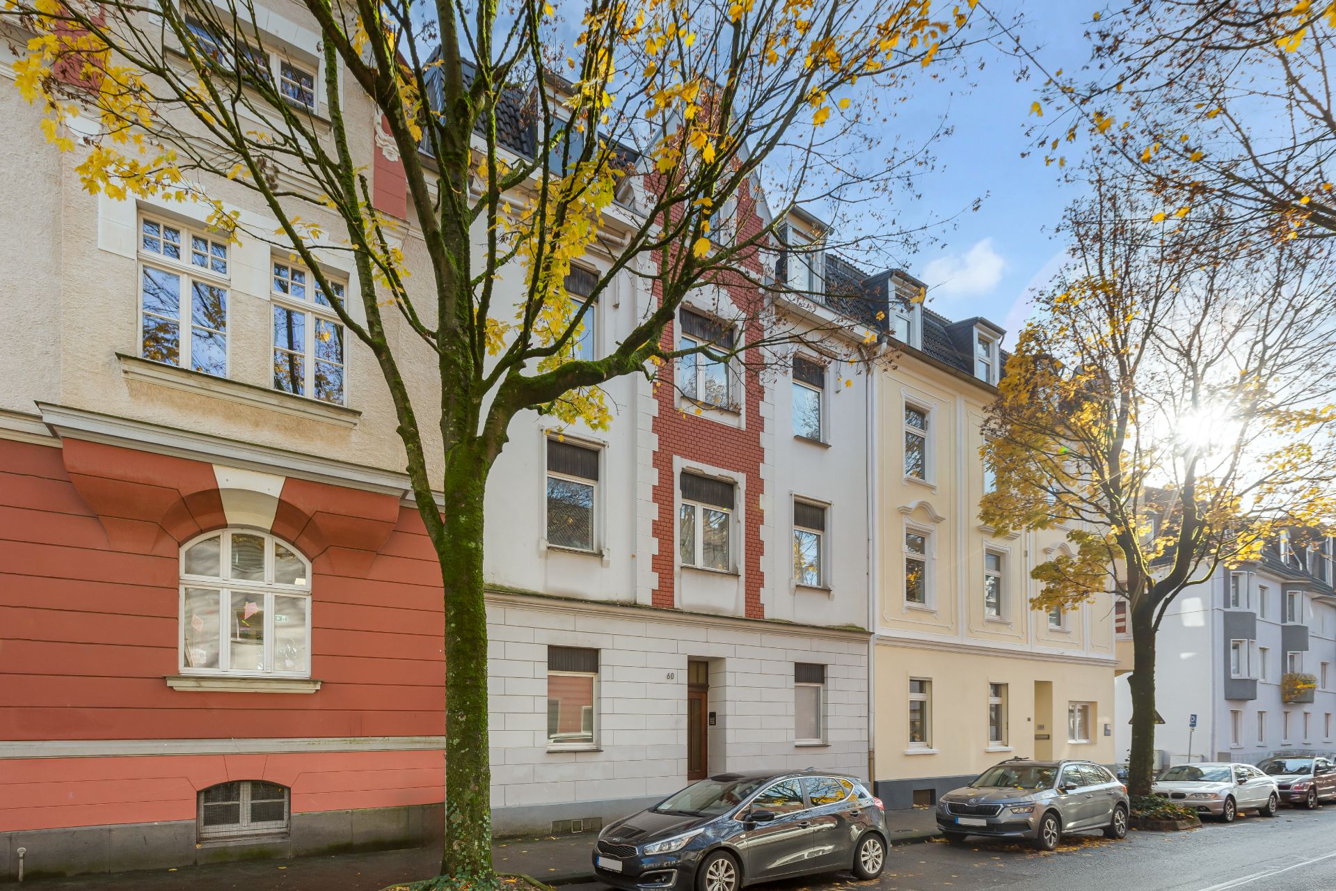 Mehrstöckiges Wohnhaus mit Bäumen und parkenden Autos an der Straße.