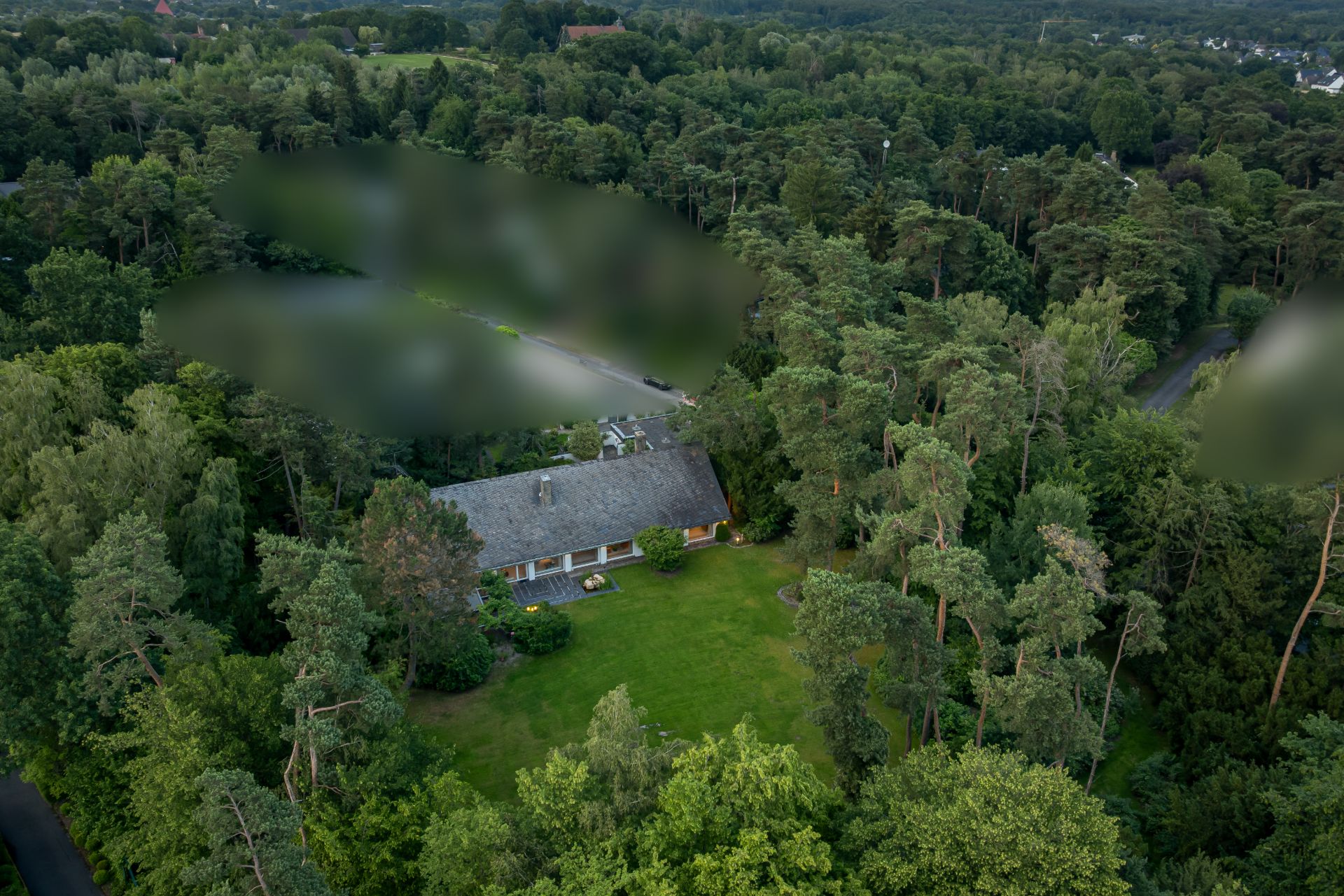 Luftaufnahme eines Hauses mit großem Garten, umgeben von dichtem Wald.