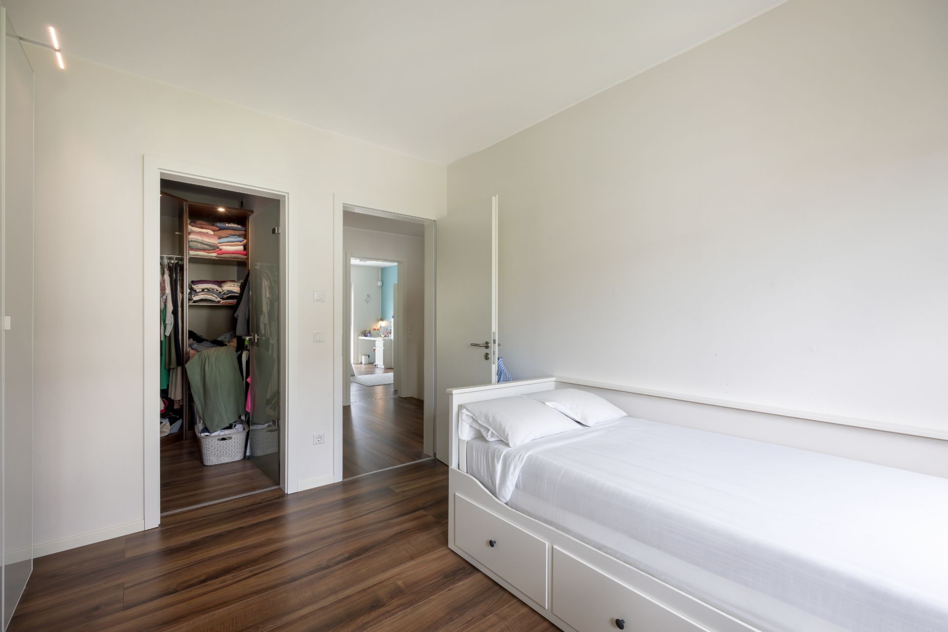 Helles Schlafzimmer mit Einzelbett, Holzboden und offenem Kleiderschrank.
