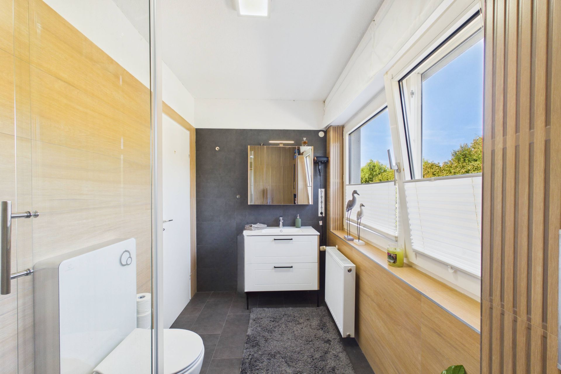 Modernes Badezimmer mit großem Fenster, Waschbecken, Spiegel und WC.