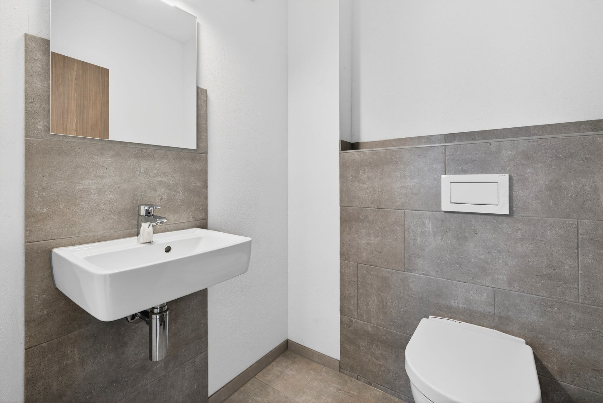 Modernes Bad mit Wandwaschbecken, Spiegel und Wand-WC, grau gefliest.