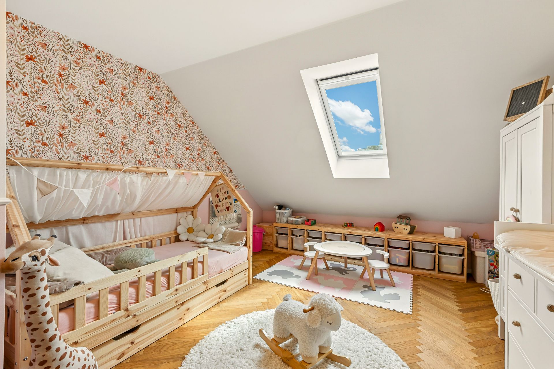 Helles Kinderzimmer mit Holzbett, Spielzeug, Teppich und Dachfenster.