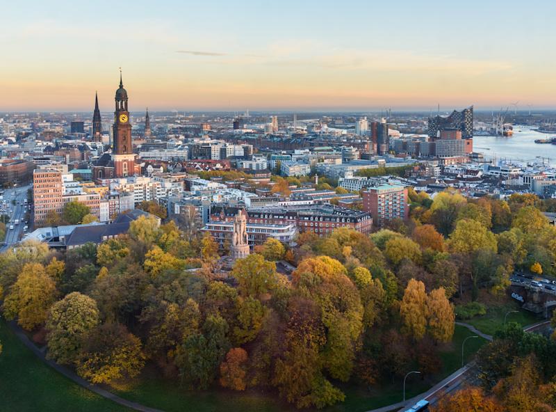 Blick über eine Stadt mit vielen Bäumen und einem Fluss im Hintergrund.