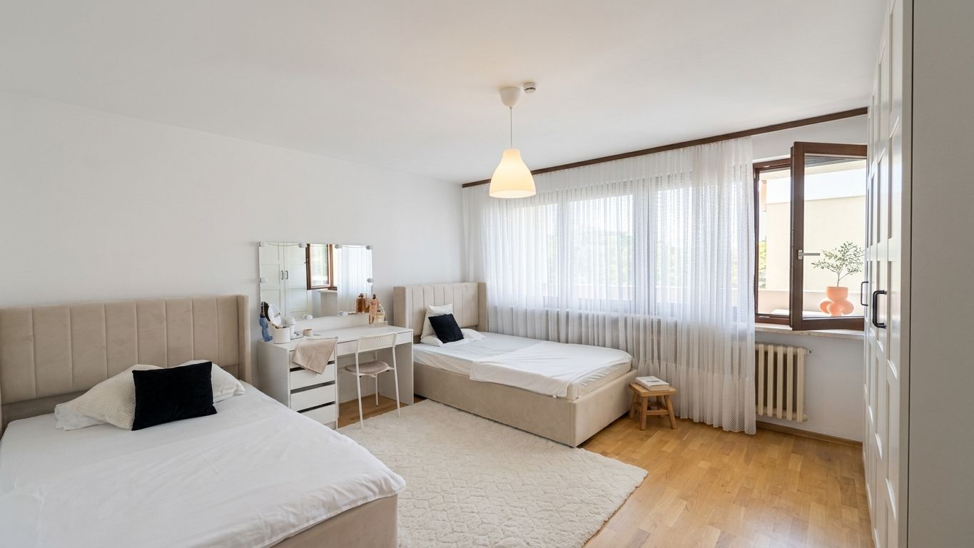 Helles Schlafzimmer mit zwei Einzelbetten, Schminktisch, Teppich und großem Fenster mit Gardinen.