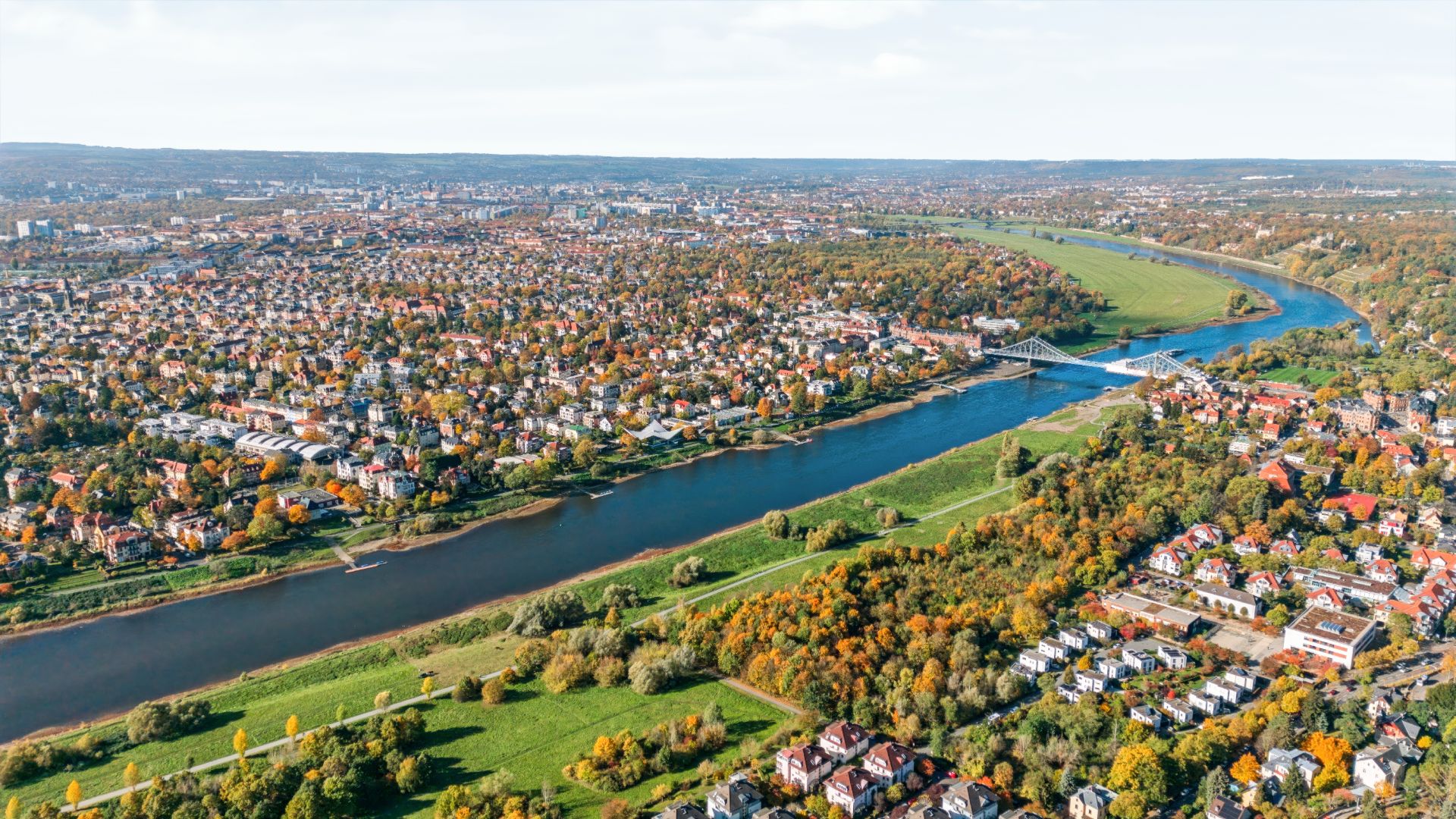Luftaufnahme einer Stadt mit Fluss, Brücke und vielen Wohnhäusern im Grünen.