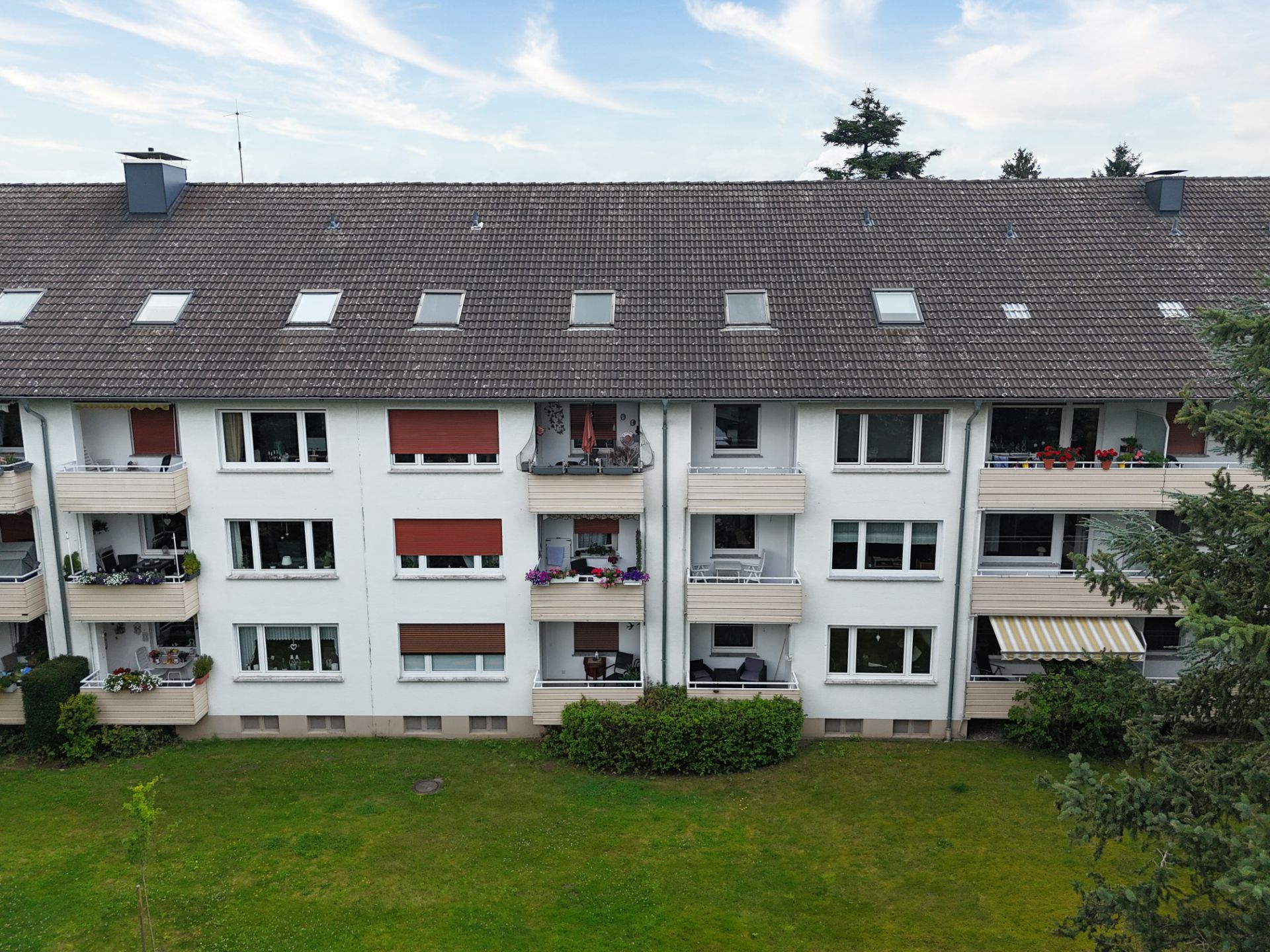 Mehrfamilienhaus mit Balkonen, weißen Fassaden und gepflegtem Garten im Vordergrund.
