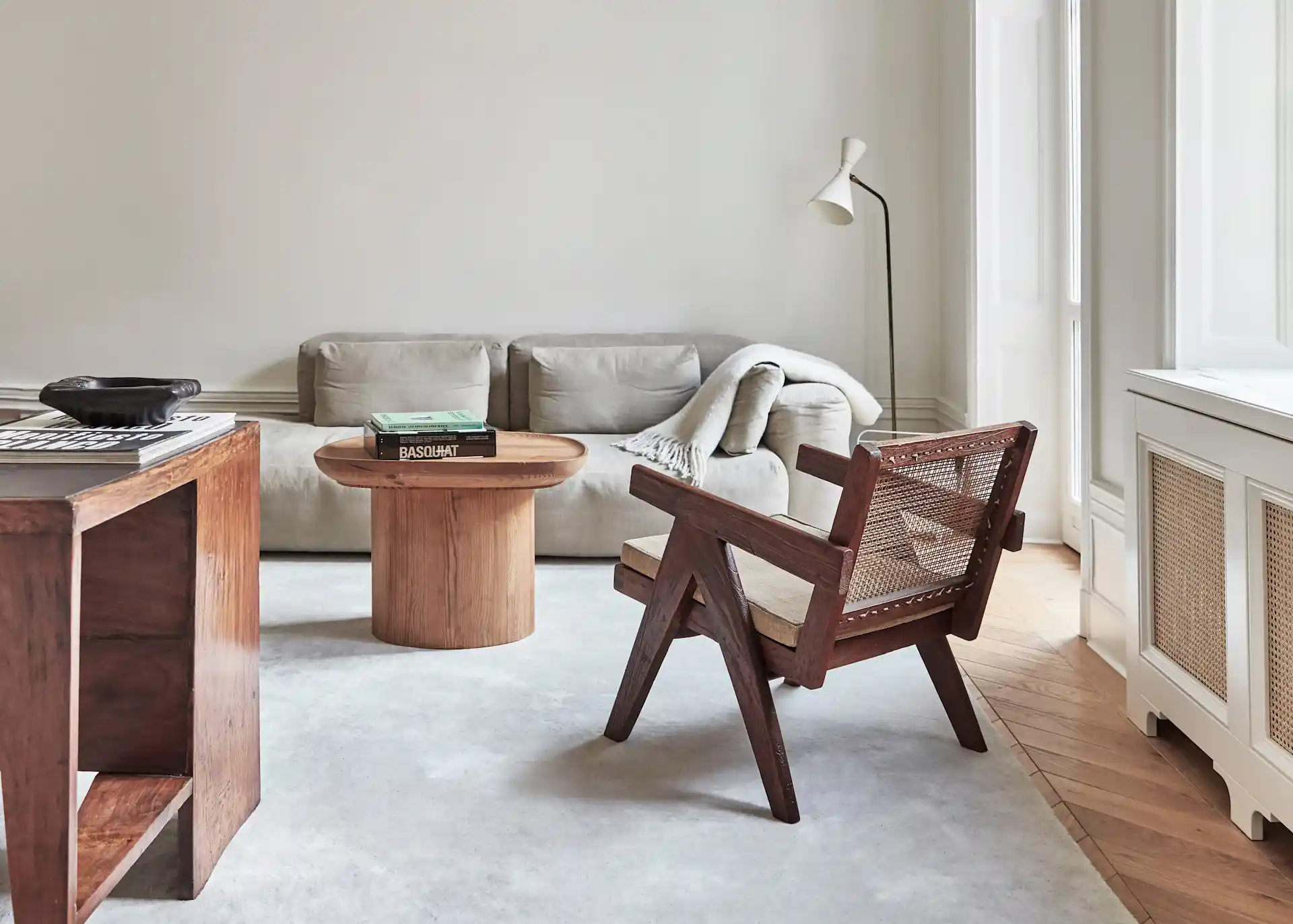 Helles Wohnzimmer mit beigem Sofa, Holztisch, Holzsessel und Stehlampe.