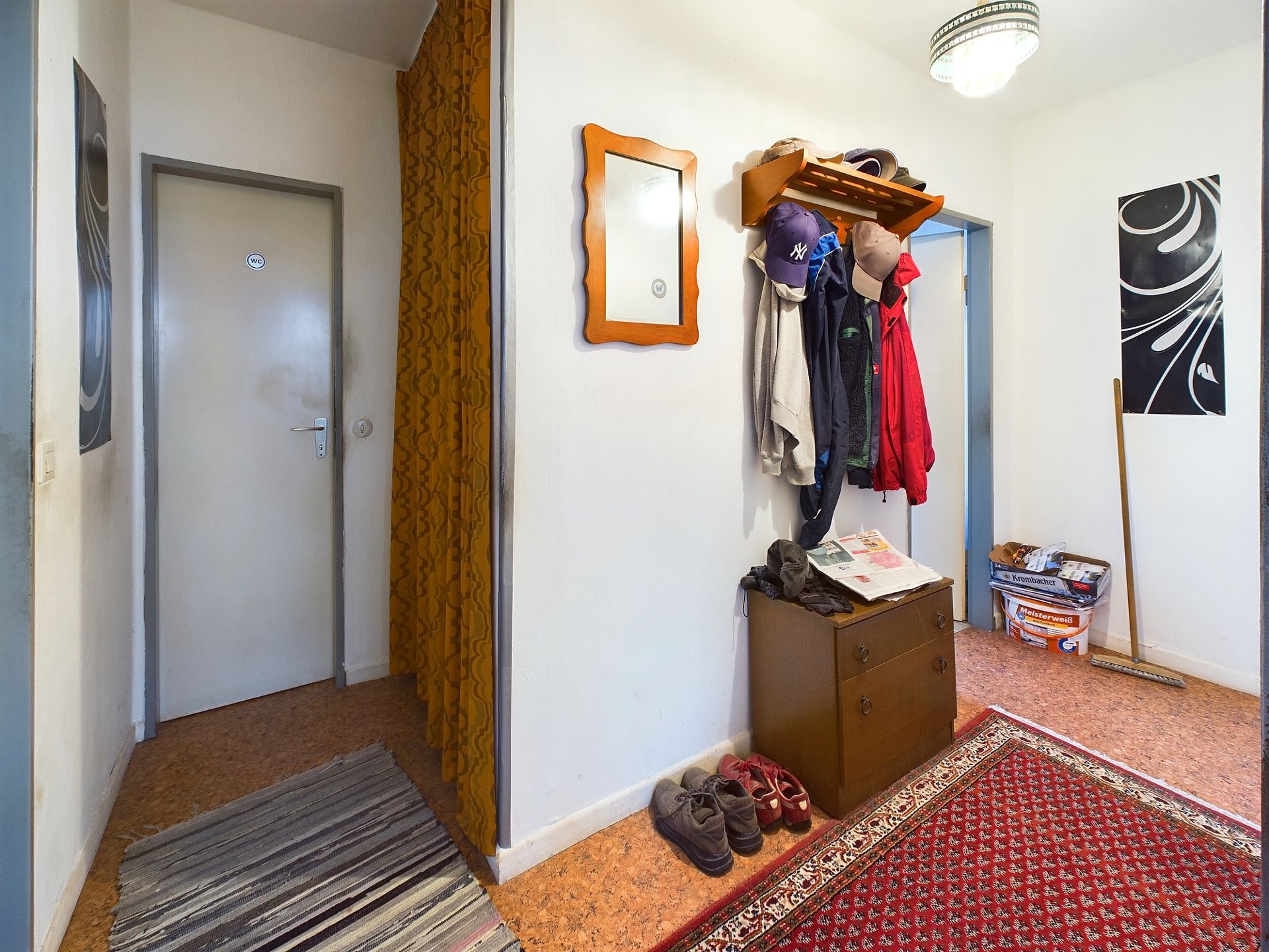 Flur mit Garderobe, Schuhen, Spiegel, Kommode und Teppich auf dem Boden.