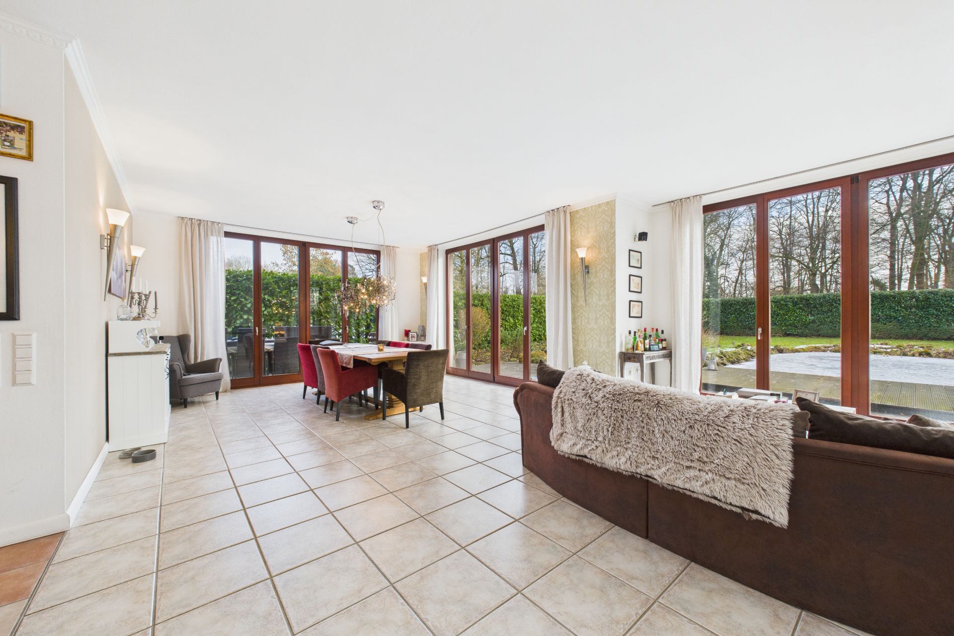 Helles Wohnzimmer mit braunem Sofa, Esstisch und großen Fenstern mit Blick auf Garten.