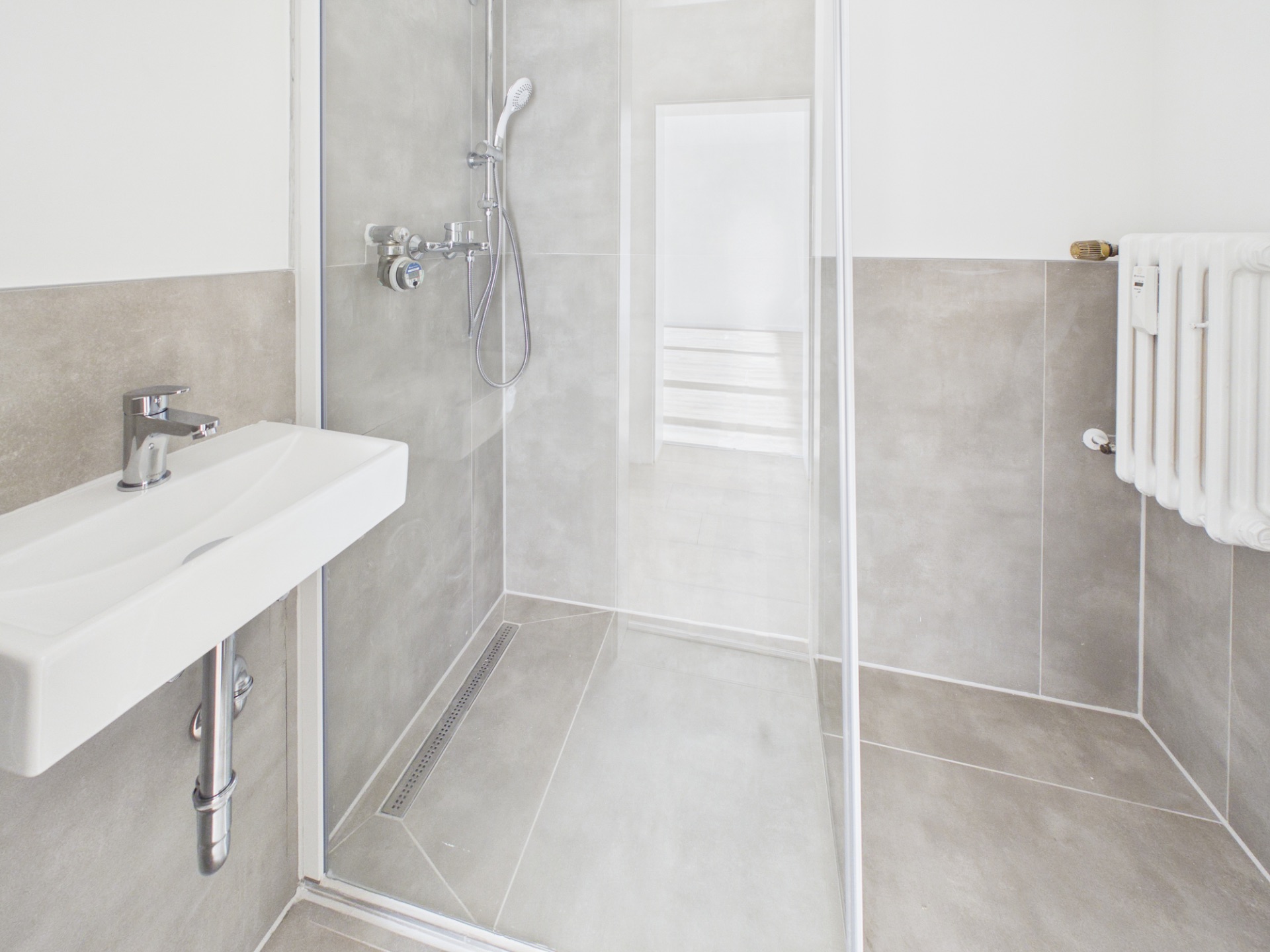 Modernes Badezimmer mit begehbarer Dusche, Waschbecken und Heizkörper.