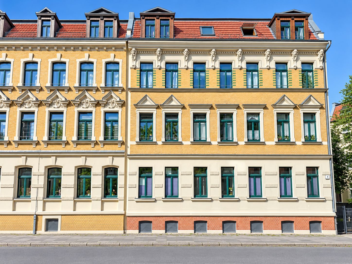 Fassade eines mehrstöckigen Wohngebäudes mit grünen Fenstern und rotem Dach.