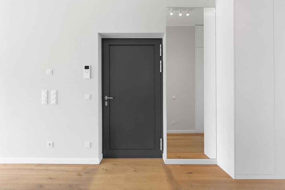 Schwarze Tür in einem hellen Flur mit Holzfußboden und großem Spiegel an der Wand.