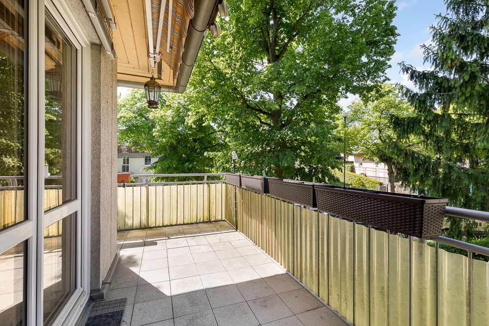 Sonniger Balkon mit Metallgeländer und Blick auf grüne Bäume.