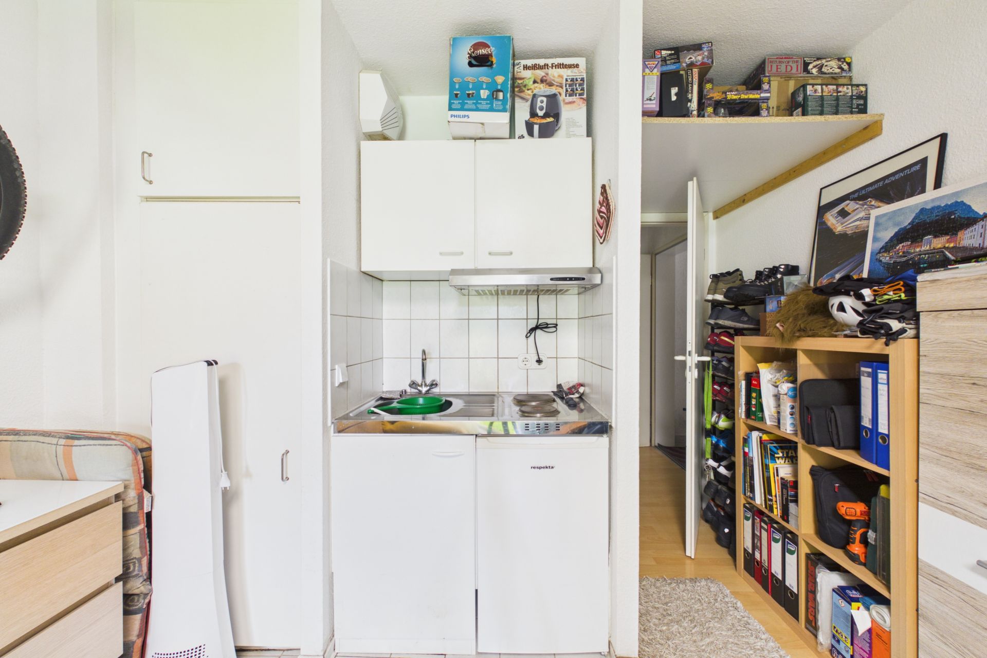 Kleine Küchenzeile mit Spüle, Herd und weißen Schränken in einem Wohnzimmer.