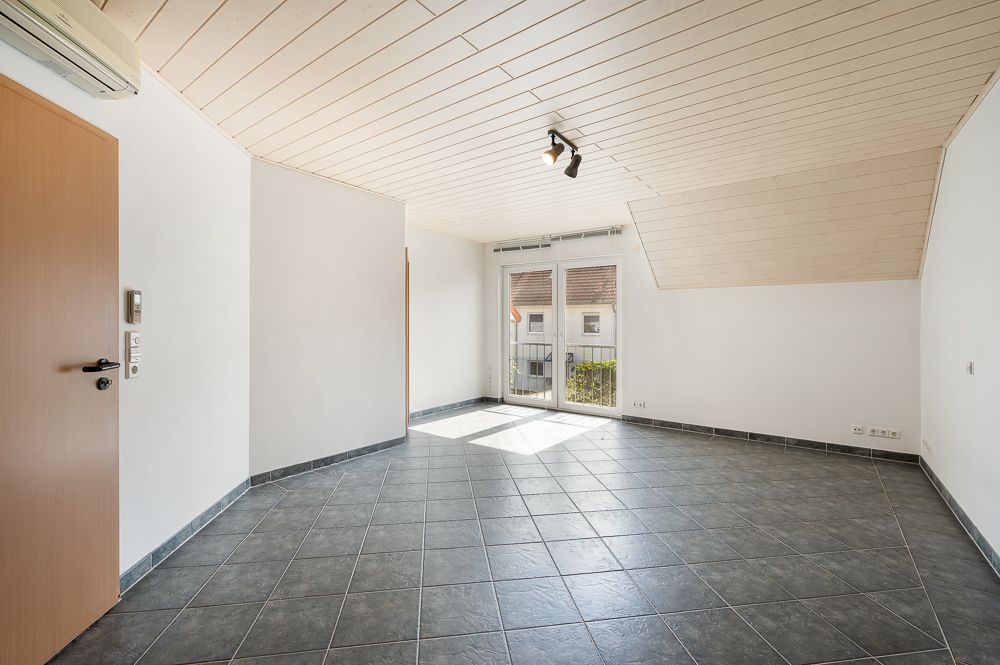 Heller leerer Raum mit Fliesenboden, weißen Wänden und Glastür zu einem kleinen Balkon.