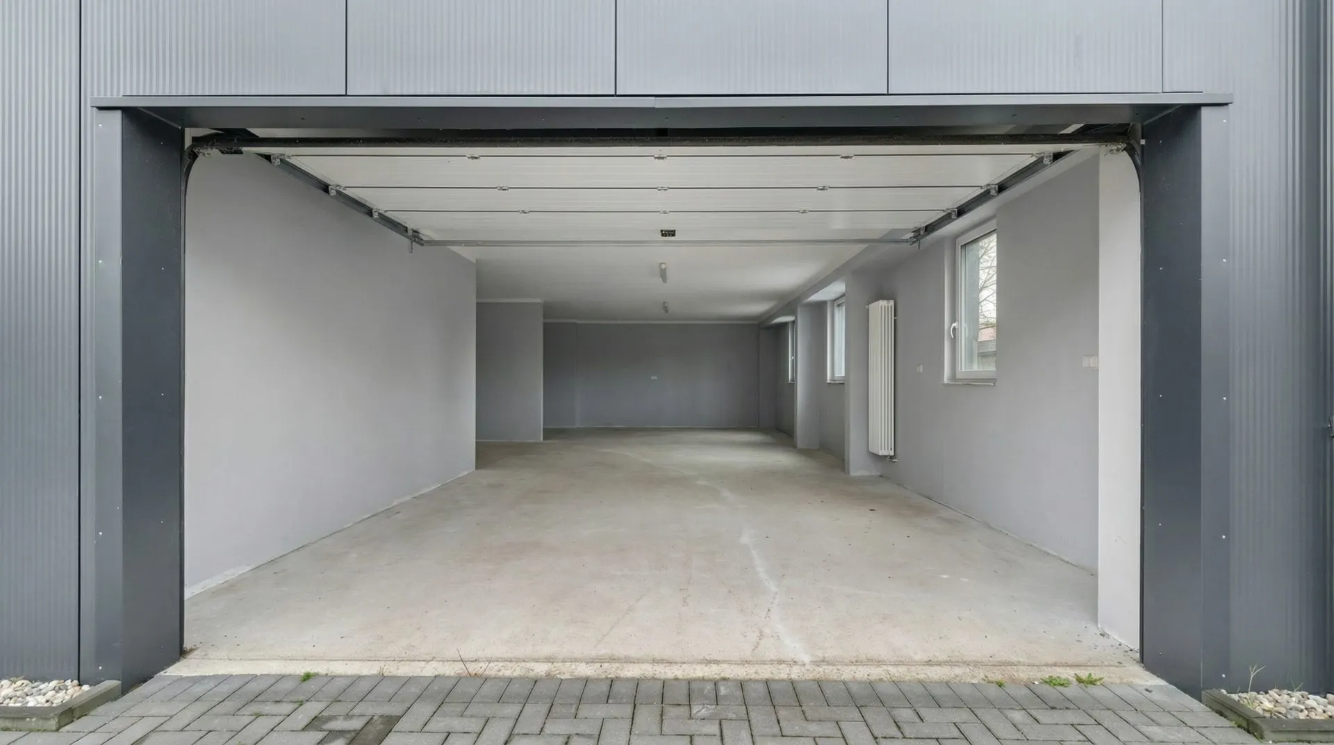 Leere Doppelgarage mit grauen Wänden und Fenstern, Blick vom offenen Tor nach innen.
