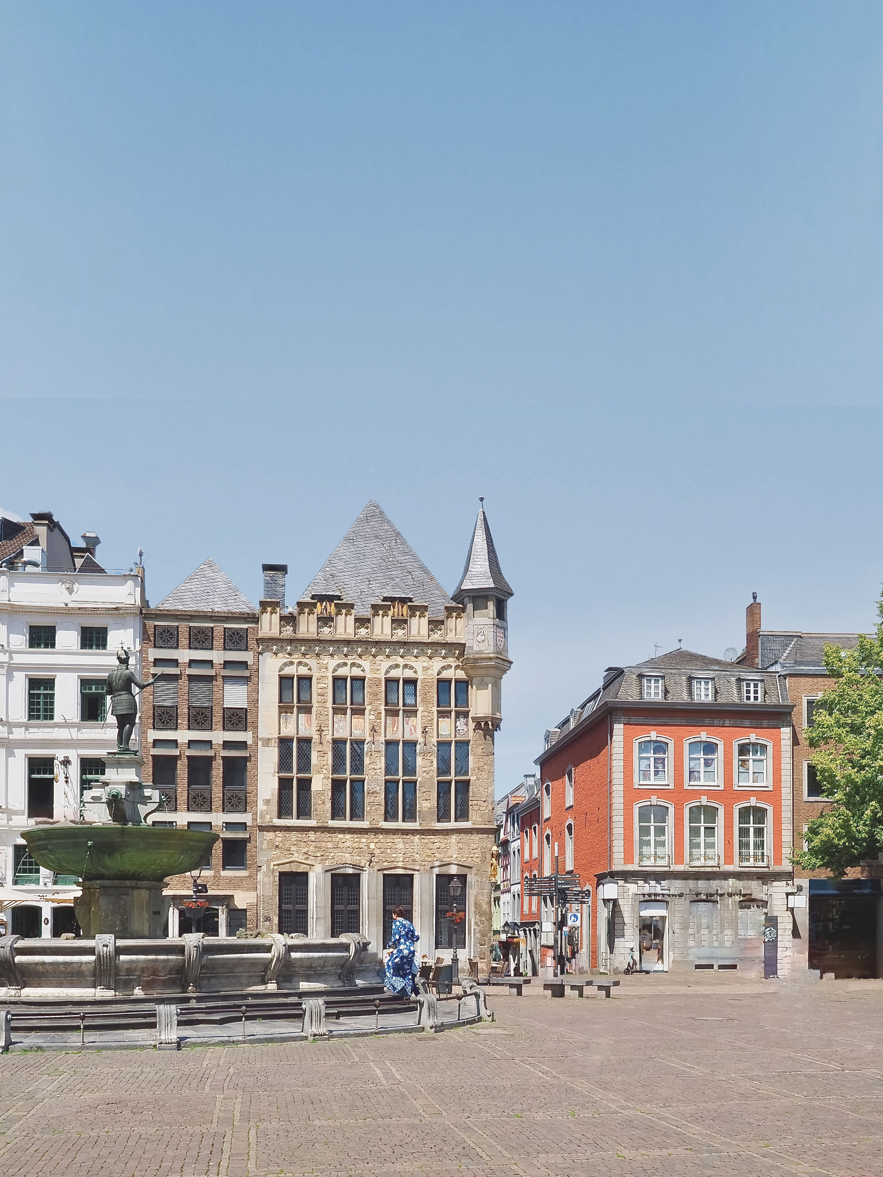 Historischer Platz mit Brunnen und mehrstöckigen Wohngebäuden bei sonnigem Wetter.
