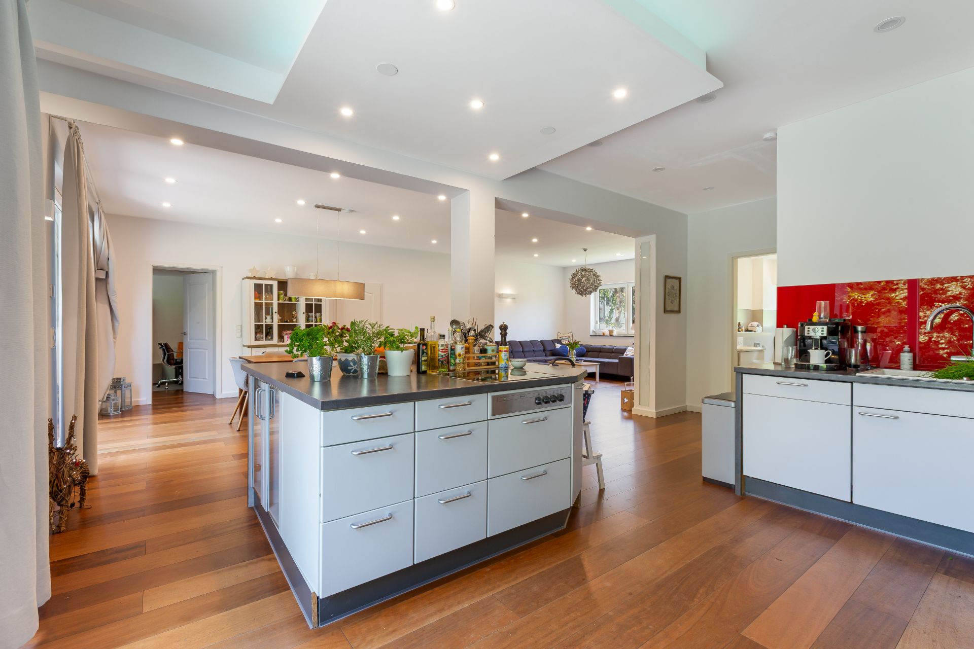 Moderne offene Küche mit großem Kücheninsel, Holzfußboden und Blick ins Wohnzimmer.