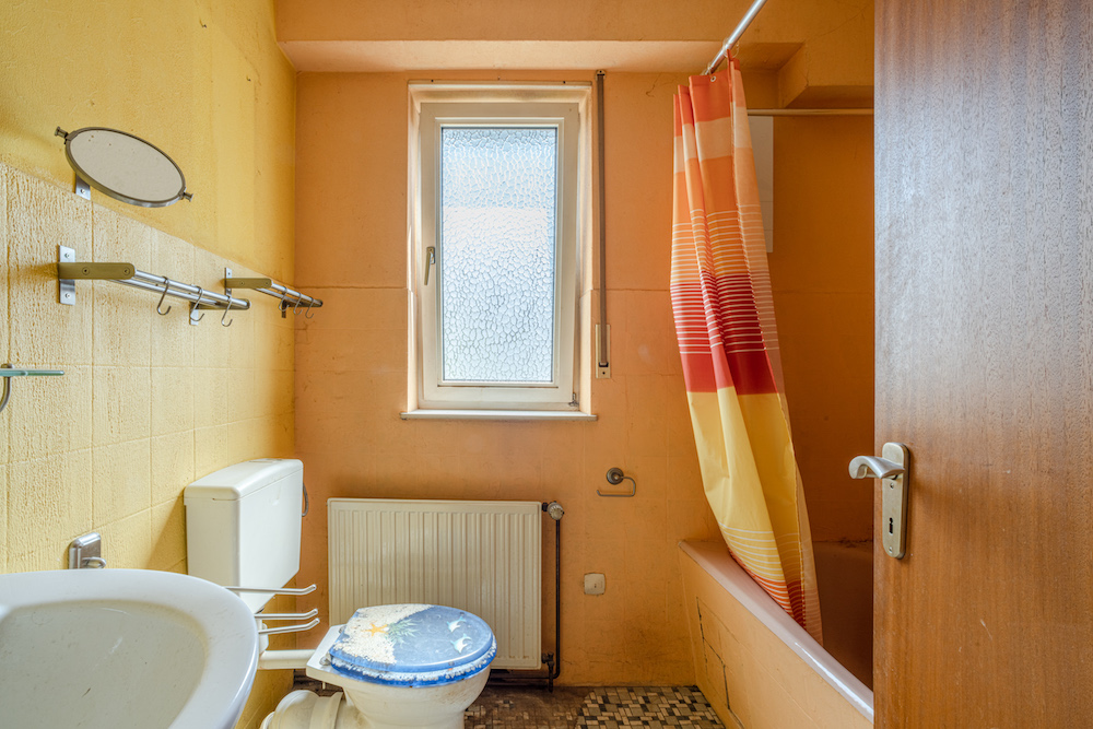 Kleines Badezimmer mit Toilette, Waschbecken, Badewanne und Duschvorhang in warmen Farben.
