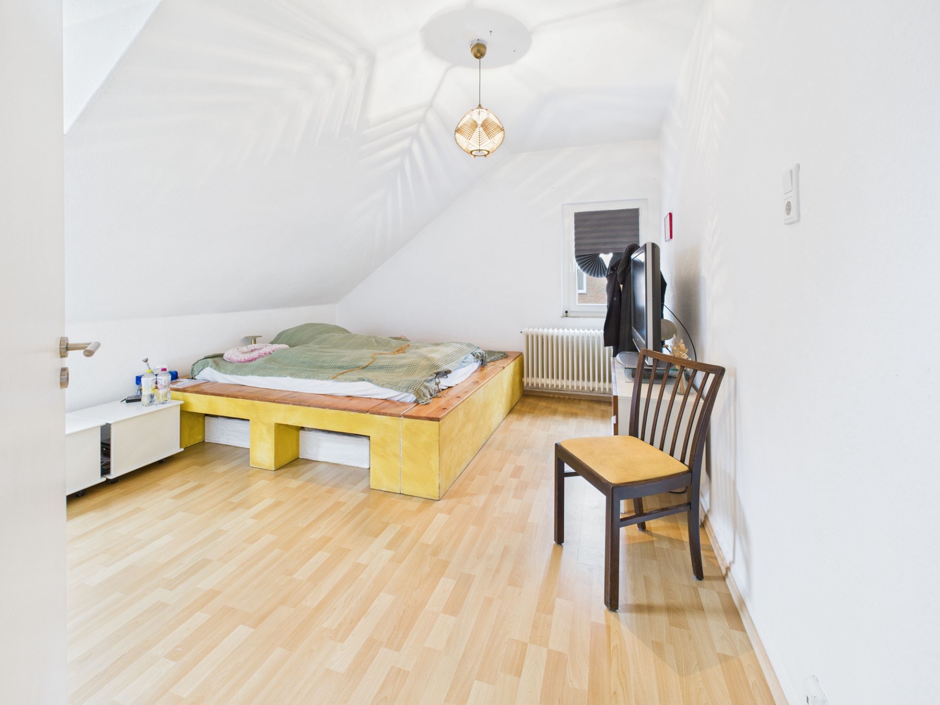 Helles Schlafzimmer mit Holzboden, großem Bett, Stuhl und Fenster unter Dachschräge.