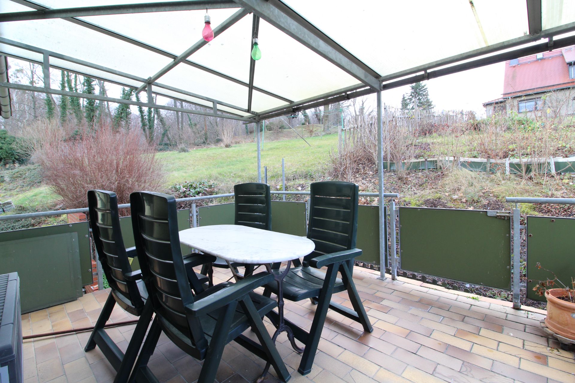 Überdachte Terrasse mit sechs schwarzen Stühlen und einem weißen Tisch, Blick auf Garten.
