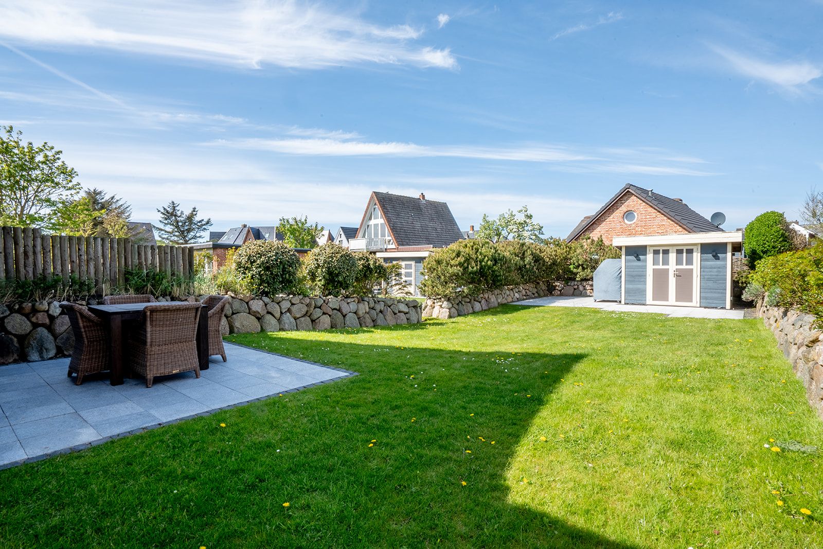 Garten mit Rasen, Terrasse mit Sitzgruppe und einem kleinen Gartenhaus im Hintergrund.