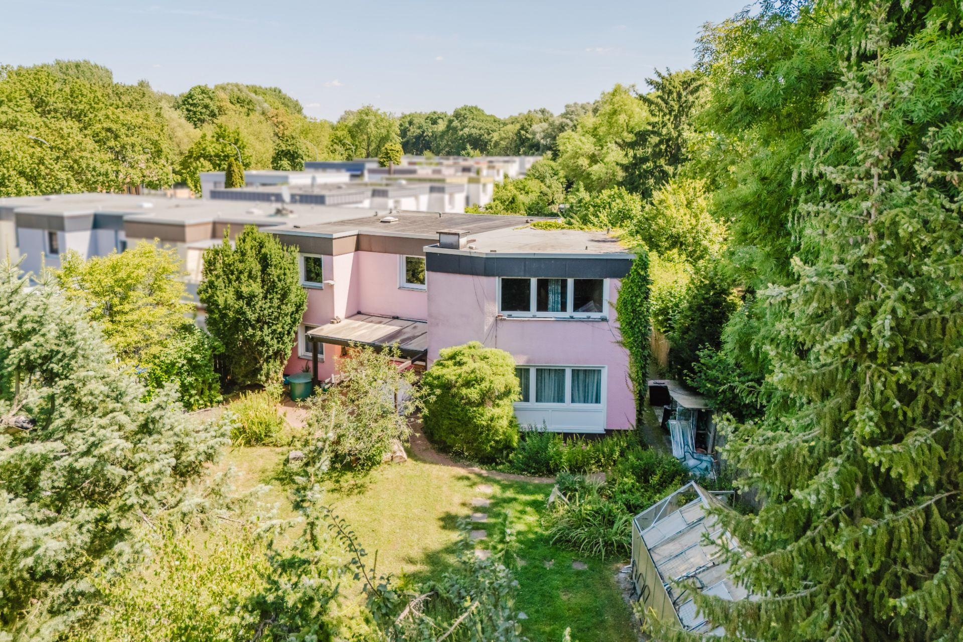 Zweistöckiges rosa Wohnhaus mit Garten, umgeben von Bäumen und Sträuchern.