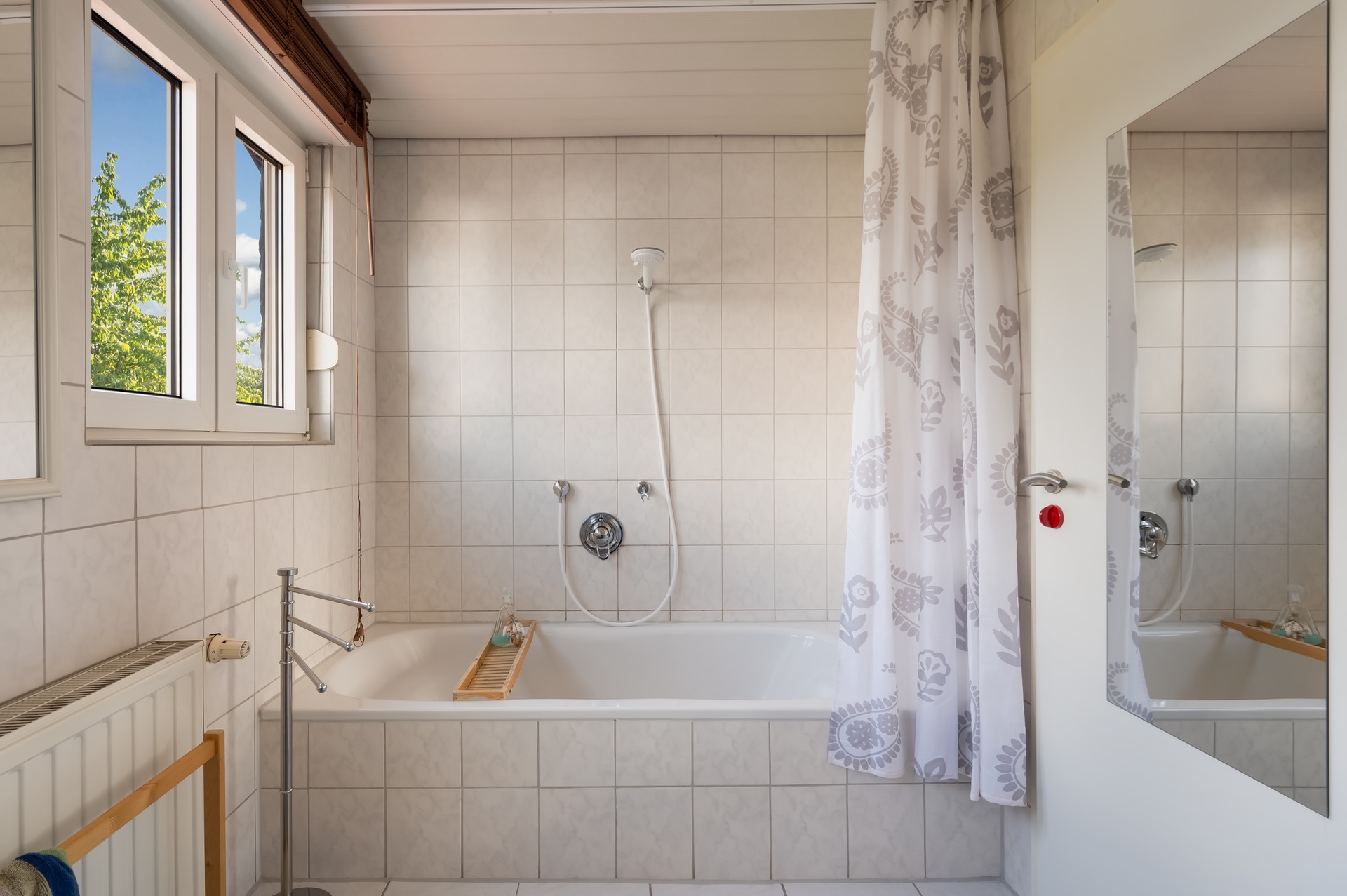Helles Badezimmer mit Badewanne, Duschvorhang und Fenster, Fliesen an Wand und Boden.