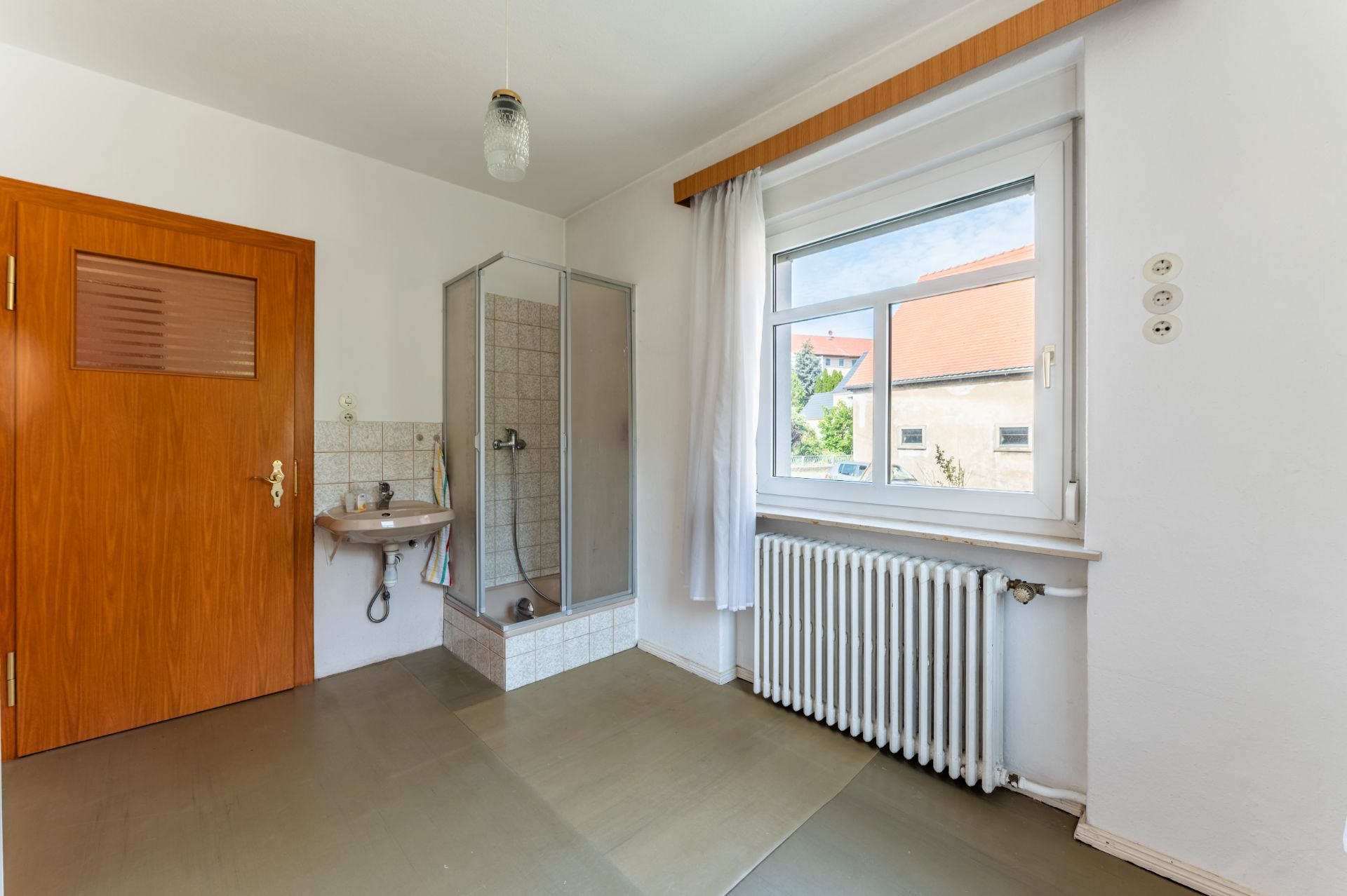 Helles Badezimmer mit Dusche, Waschbecken, Fenster und Heizkörper.