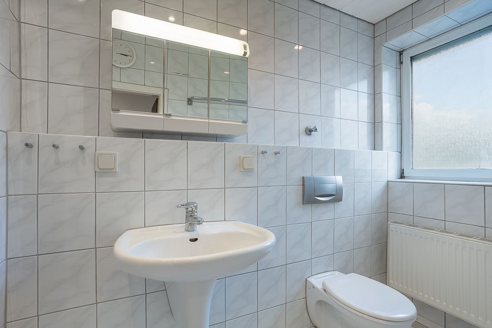 Helles Badezimmer mit Waschbecken, Spiegel, Toilette und großem Fenster.