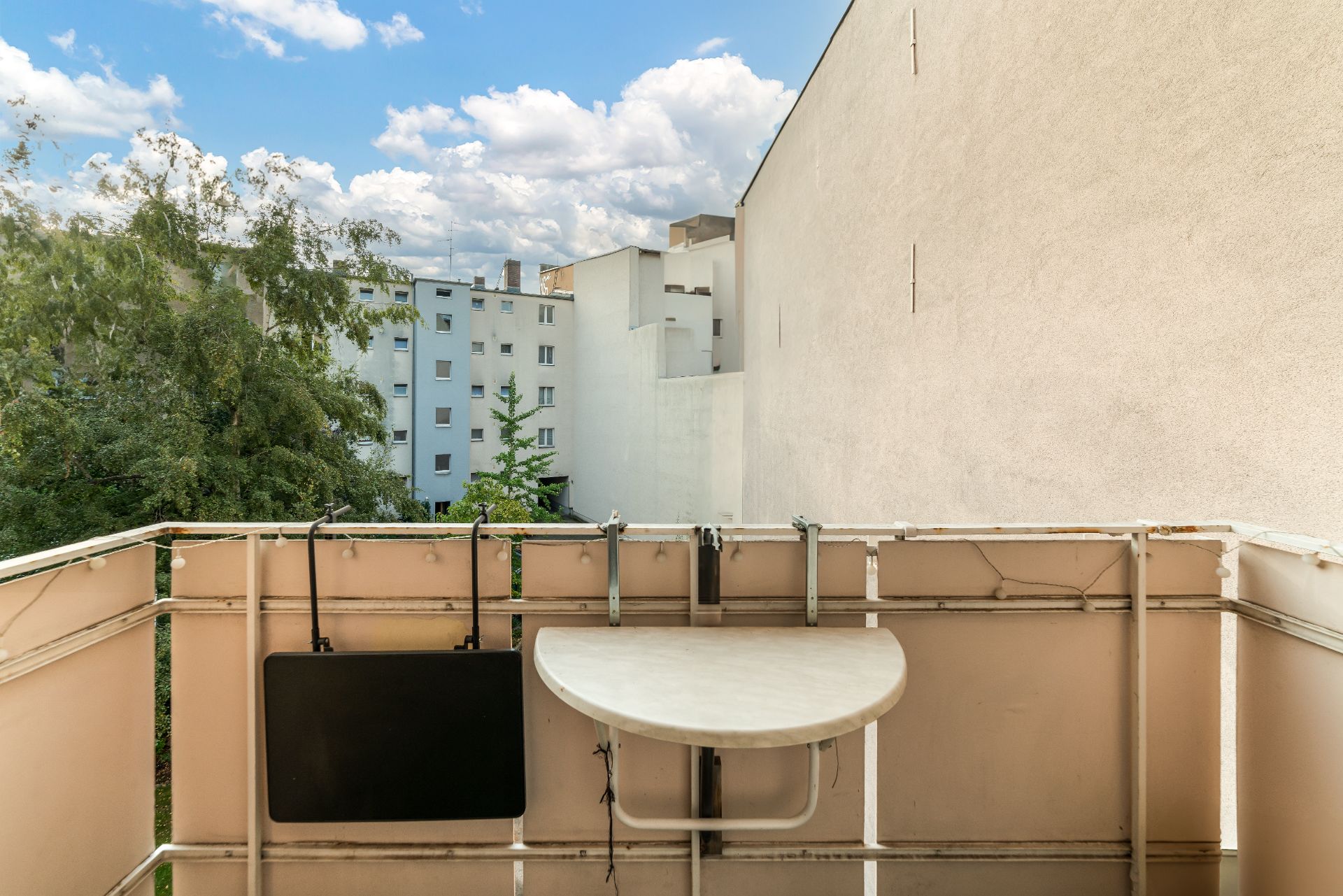 Kleiner Balkon mit klappbarem Tisch, Blick auf Bäume und benachbarte Wohnhäuser.