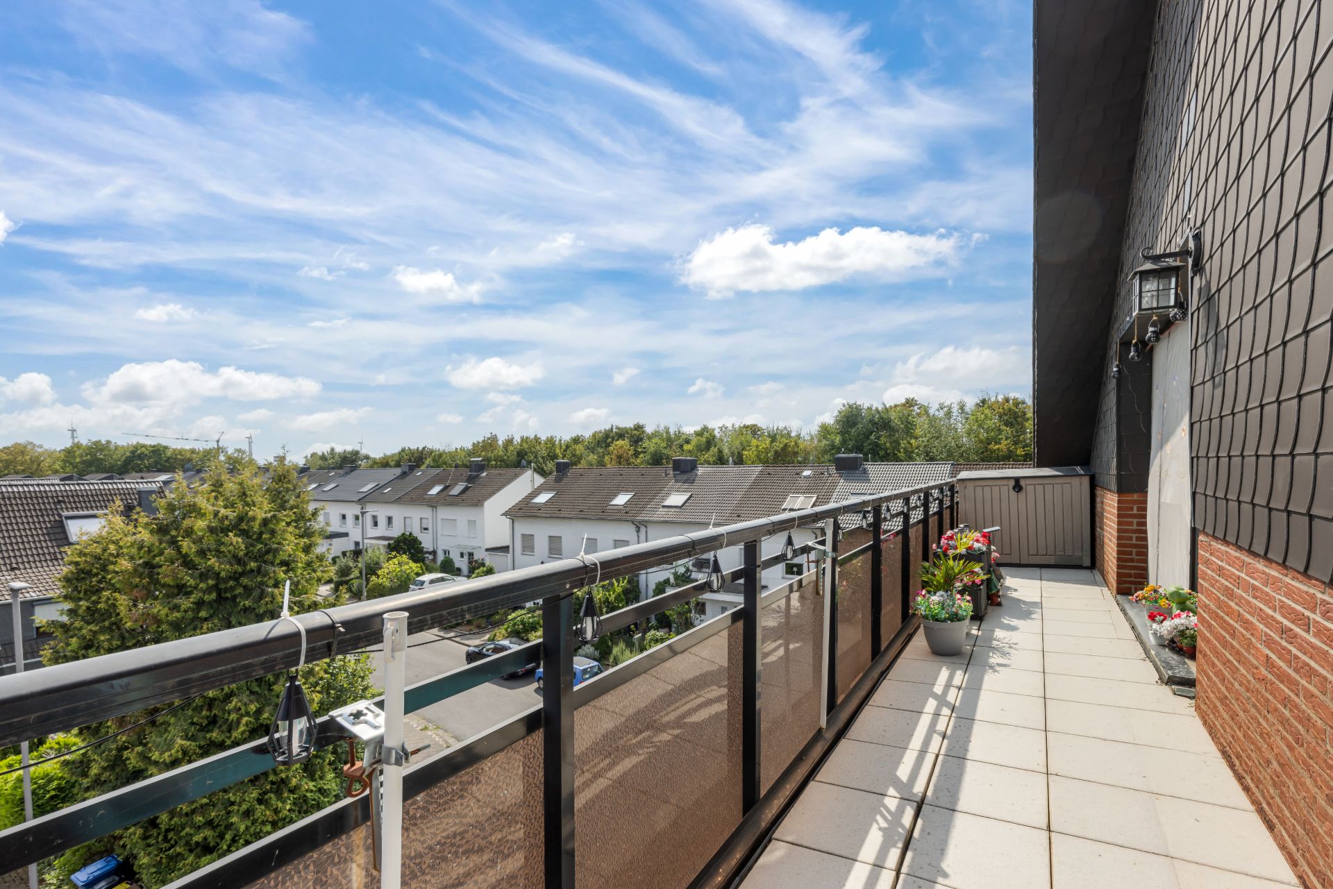 Balkon mit Blumenkästen, Blick auf Nachbarhäuser und blauen Himmel mit Wolken.