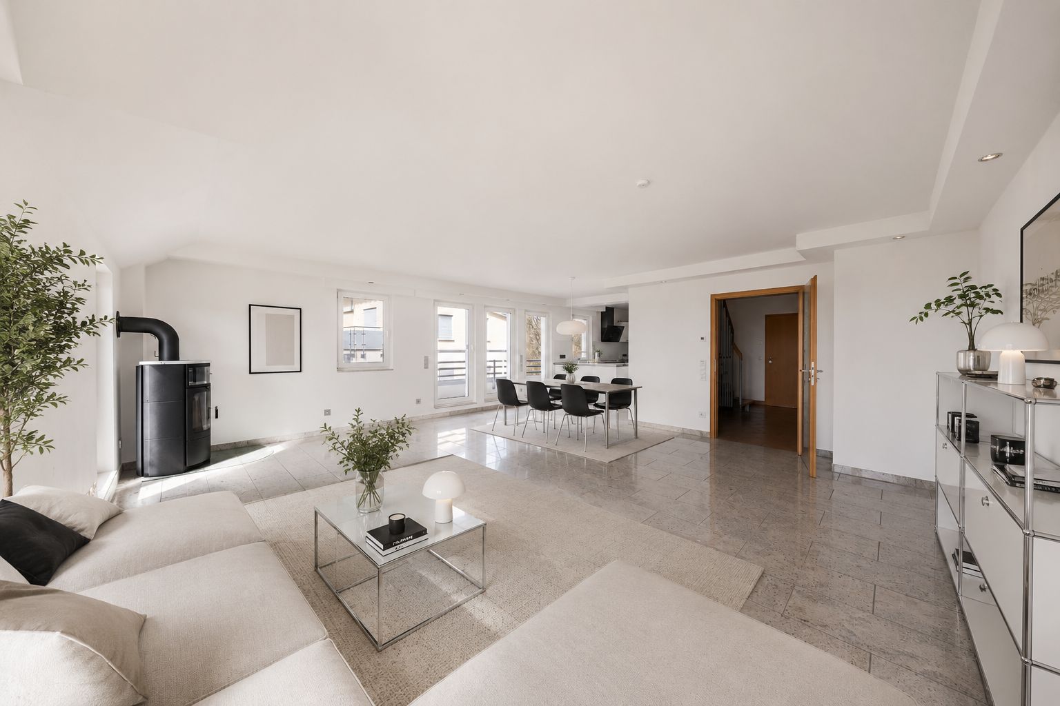 Helles Wohnzimmer mit Sofa, Esstisch, Kaminofen und großen Fenstern.
