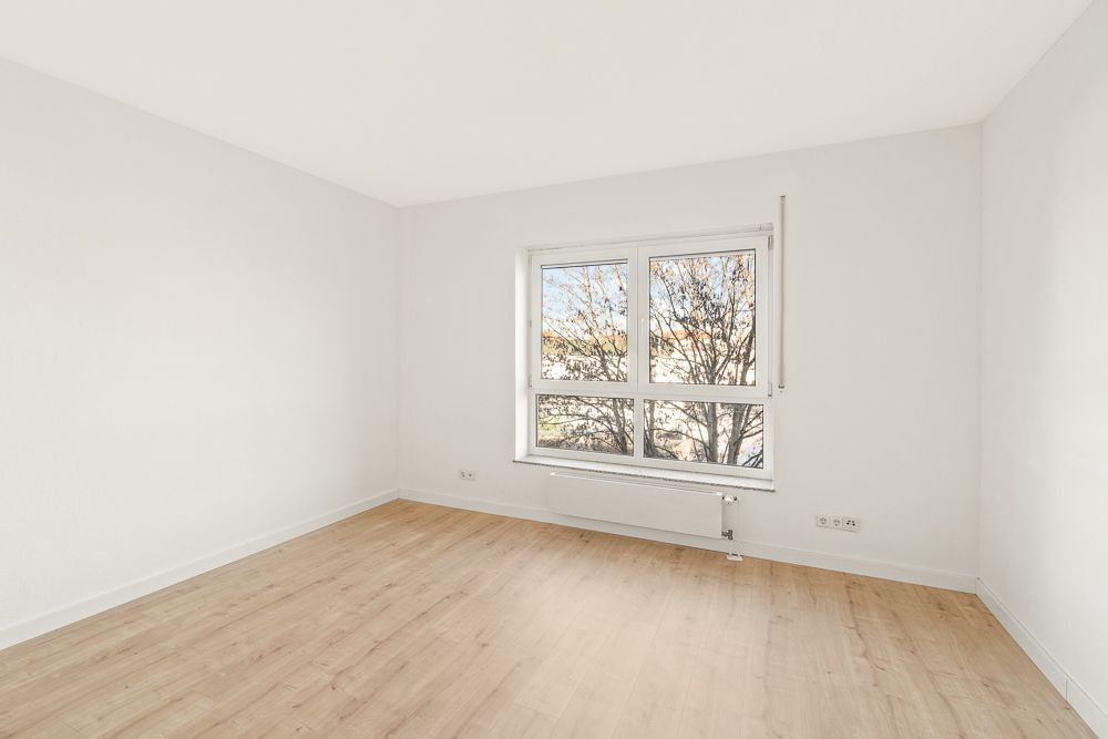 Leerer Raum mit hellem Holzfußboden und großem Fenster, weiße Wände.