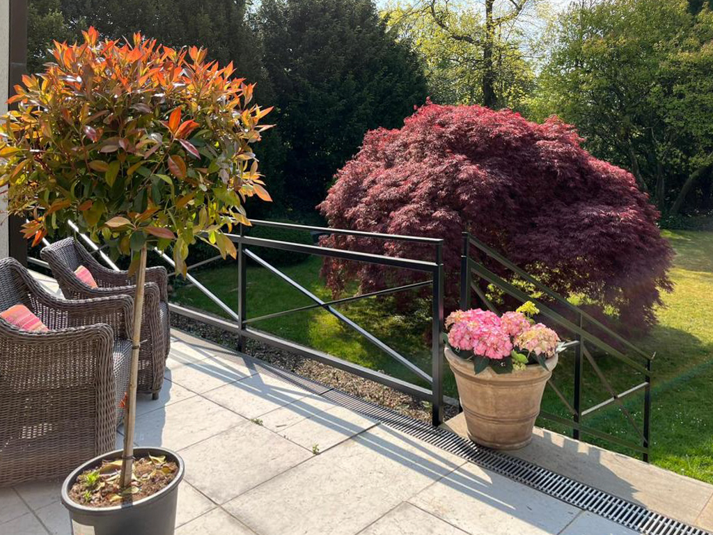 Terrasse mit zwei Rattan-Stühlen, Topfpflanzen und Blick auf einen roten Ahornbaum im Garten.