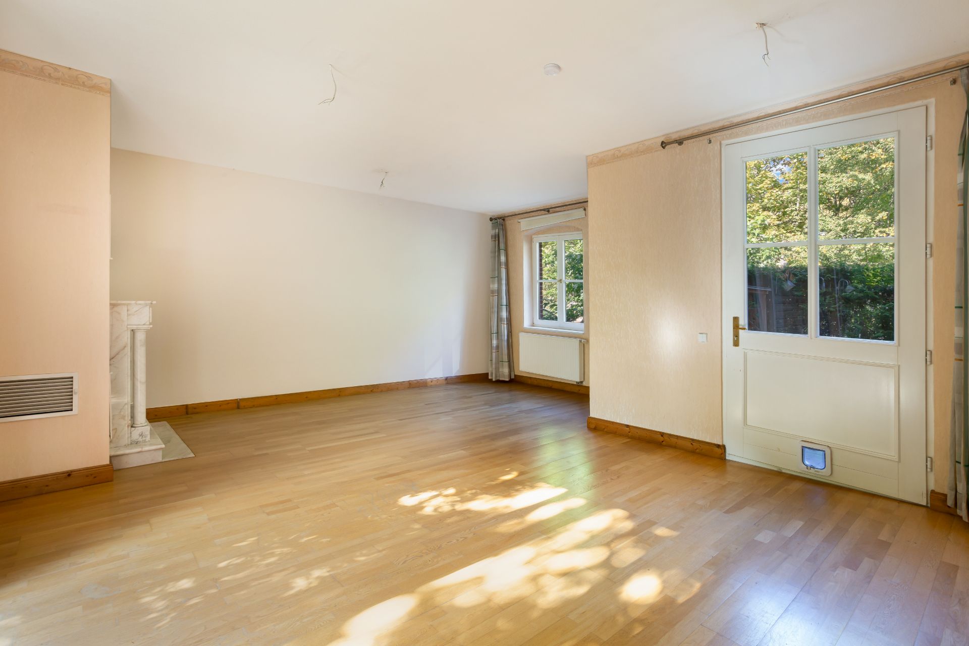 Helles Wohnzimmer mit Parkettboden, Fenstern und Glastür zum Garten.