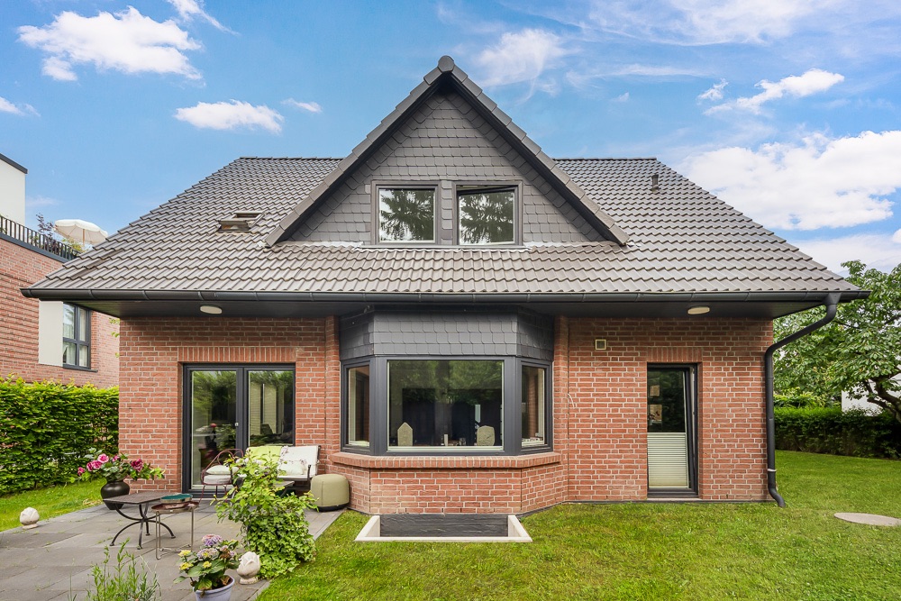 Backsteinwohnhaus mit Erker, Fensterfront und Terrasse im Garten bei Tageslicht.