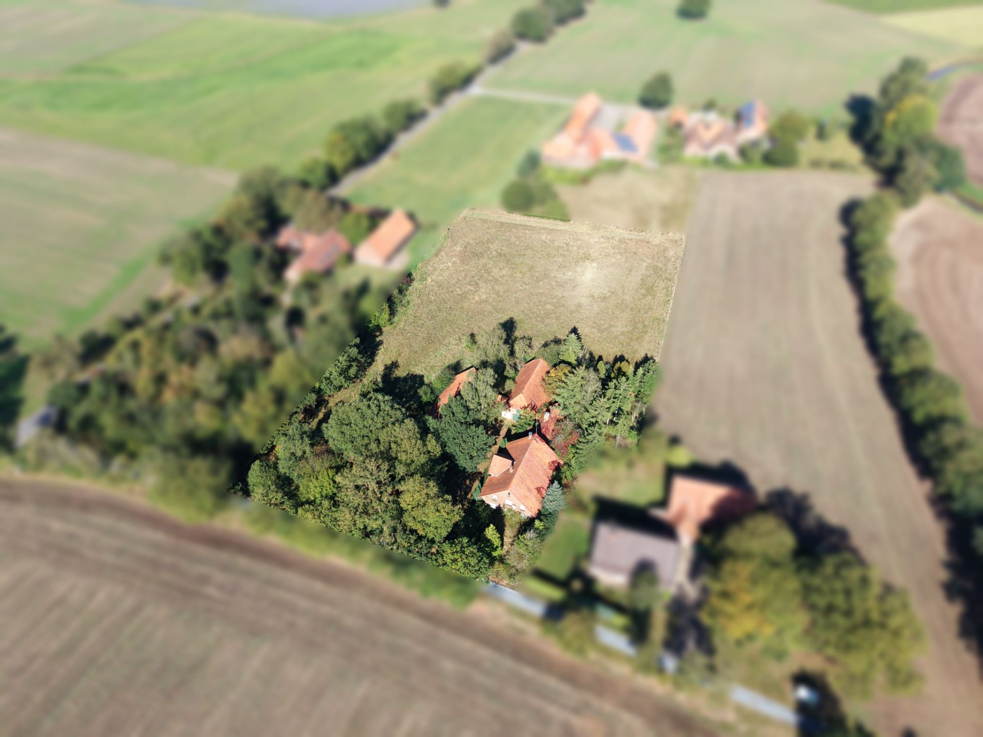 Luftaufnahme eines Hauses mit rotem Dach und Garten, umgeben von Feldern und Bäumen.