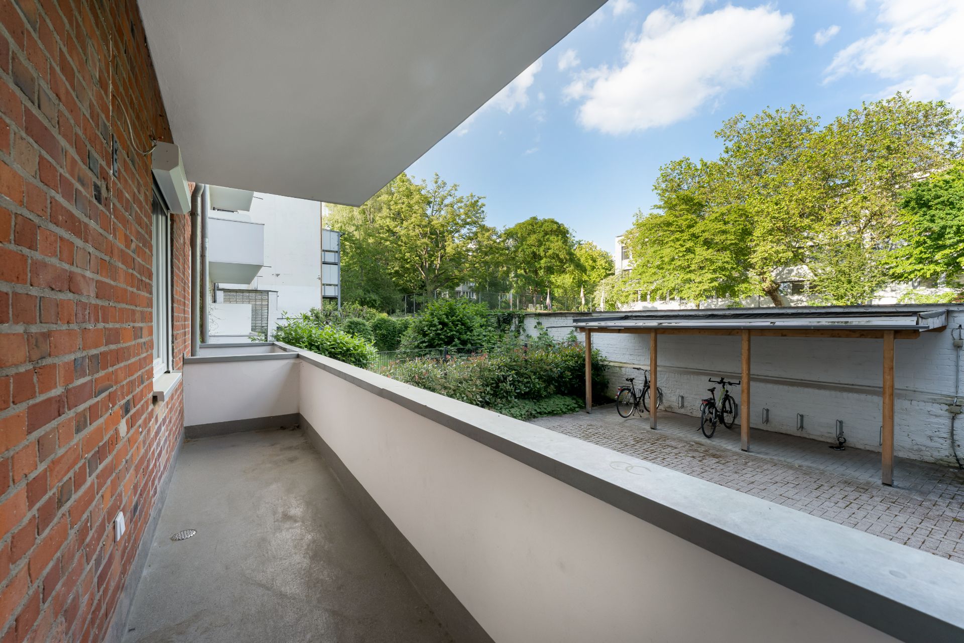Balkon mit Blick auf einen Garten und einen überdachten Fahrradstellplatz.